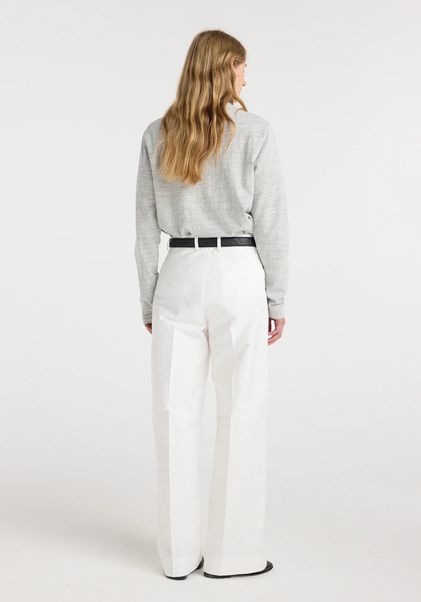 Person wearing a gray sweater and white pants on a white background