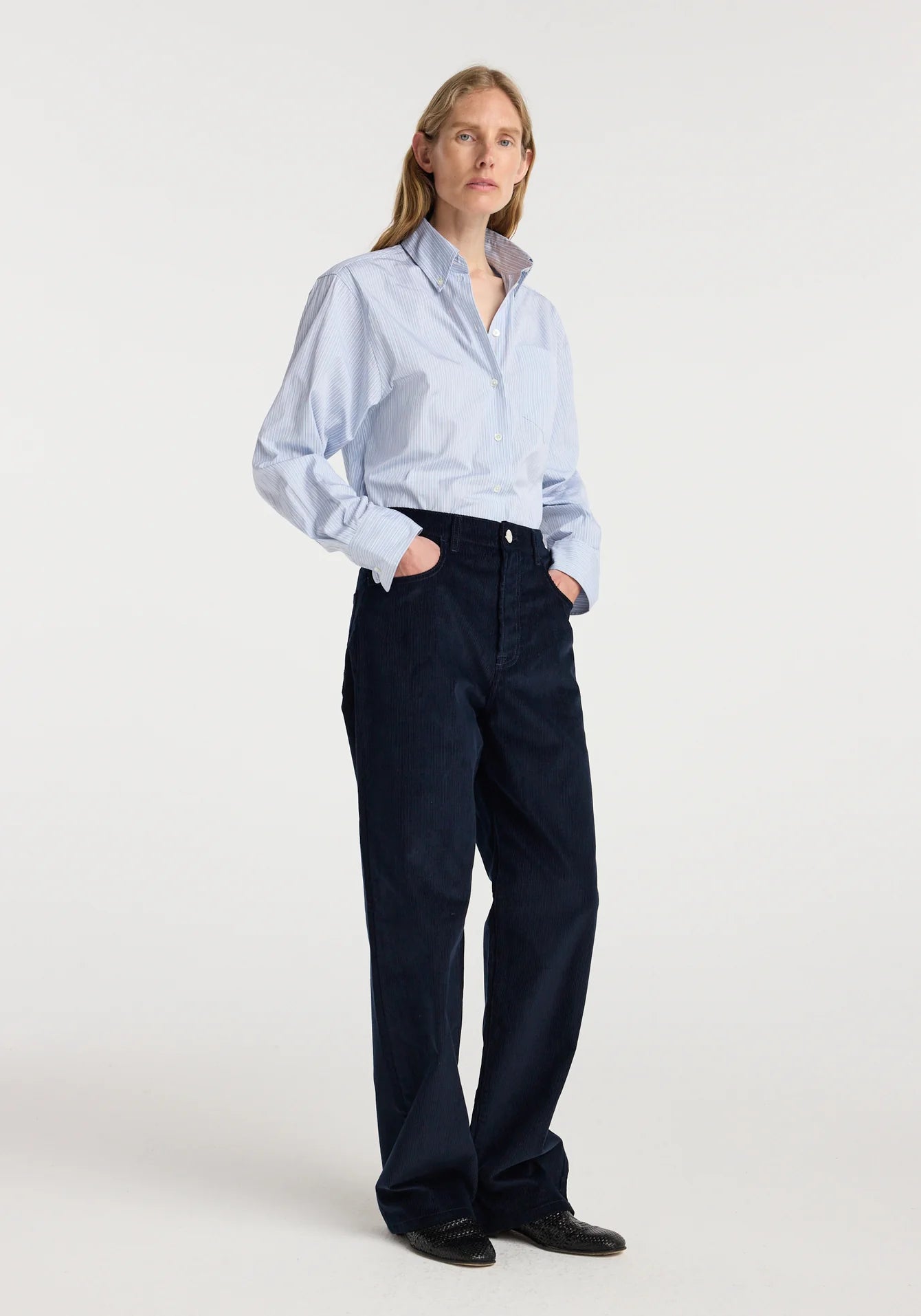 Person wearing a light blue shirt and dark pants on a white background