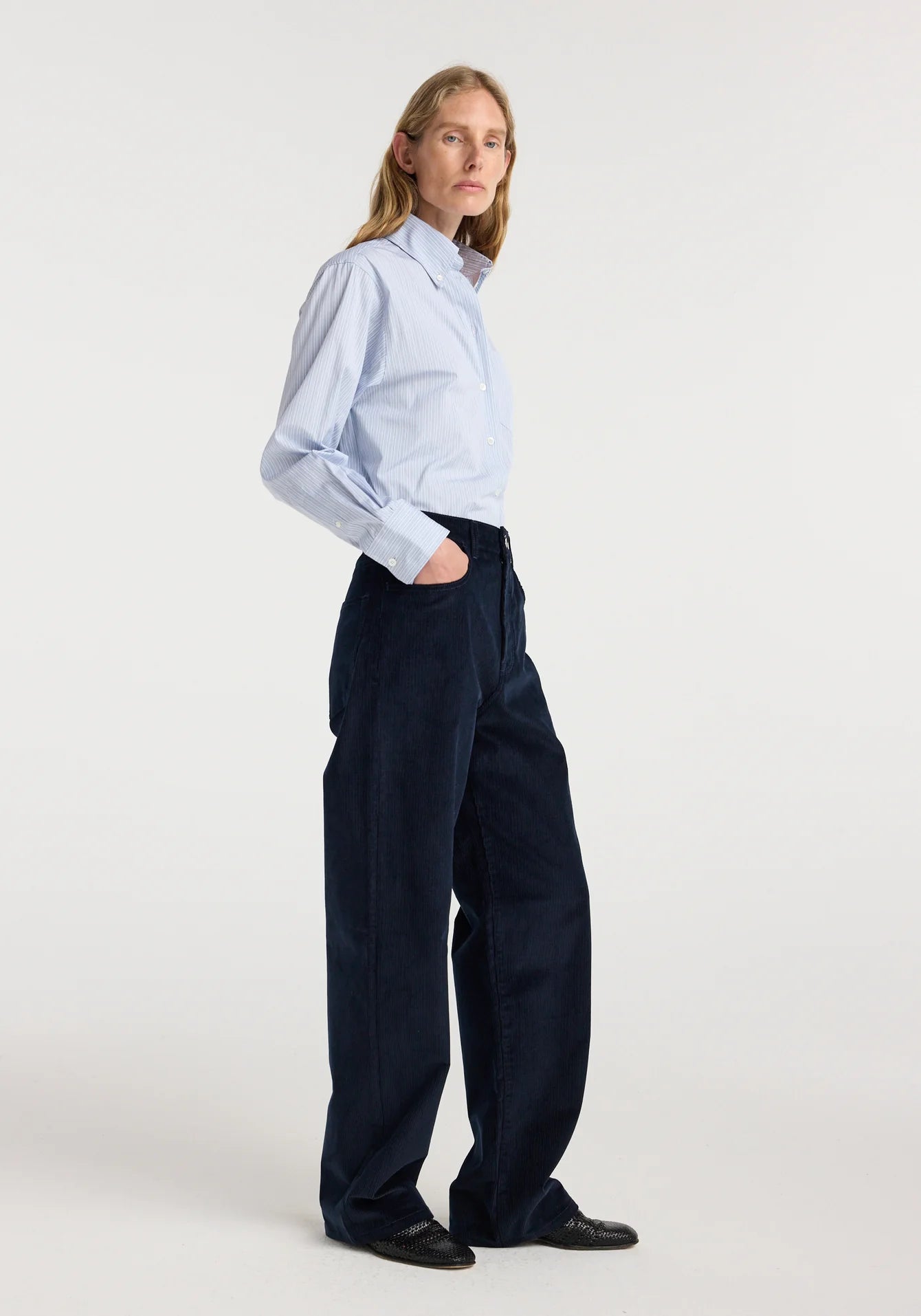 Person wearing a light blue striped shirt and dark navy pants on a white background