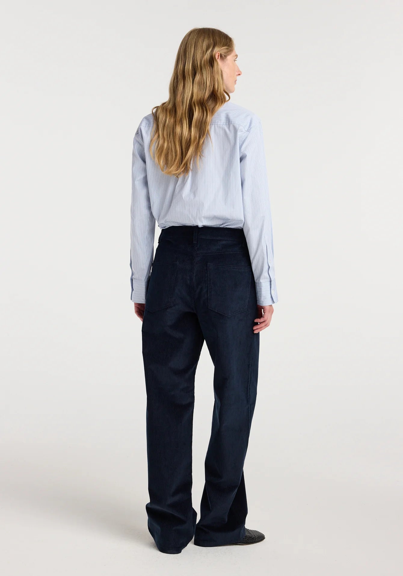 Person wearing a light blue shirt and dark pants on a white background