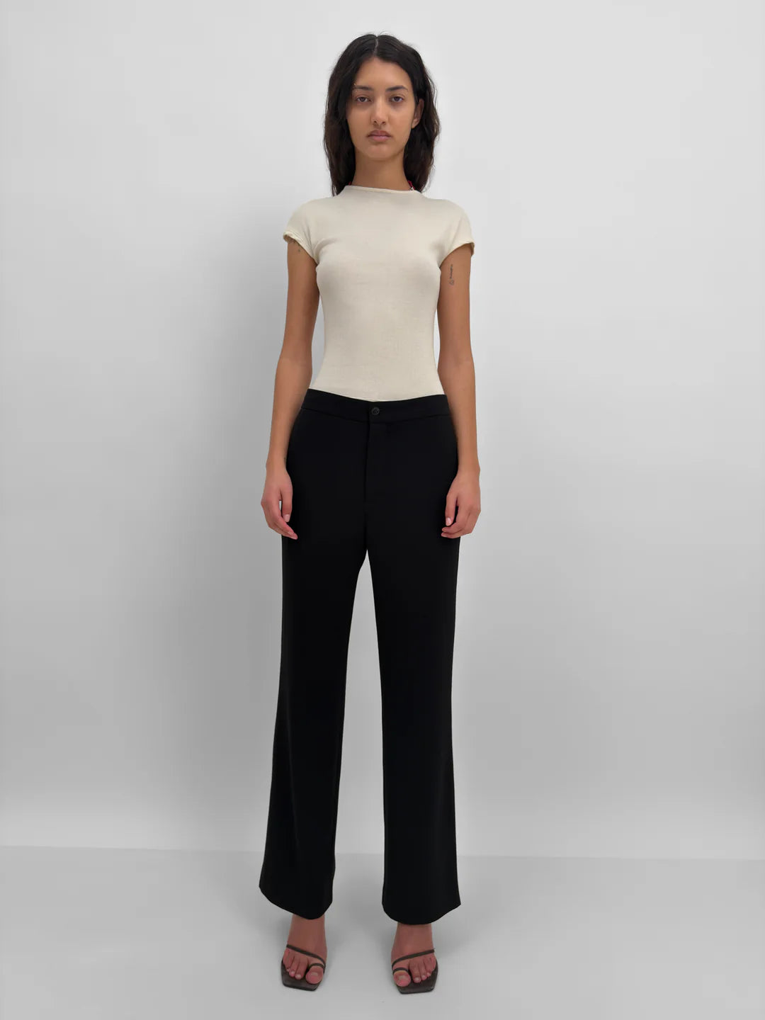 Woman wearing a beige top and black pants on a white background