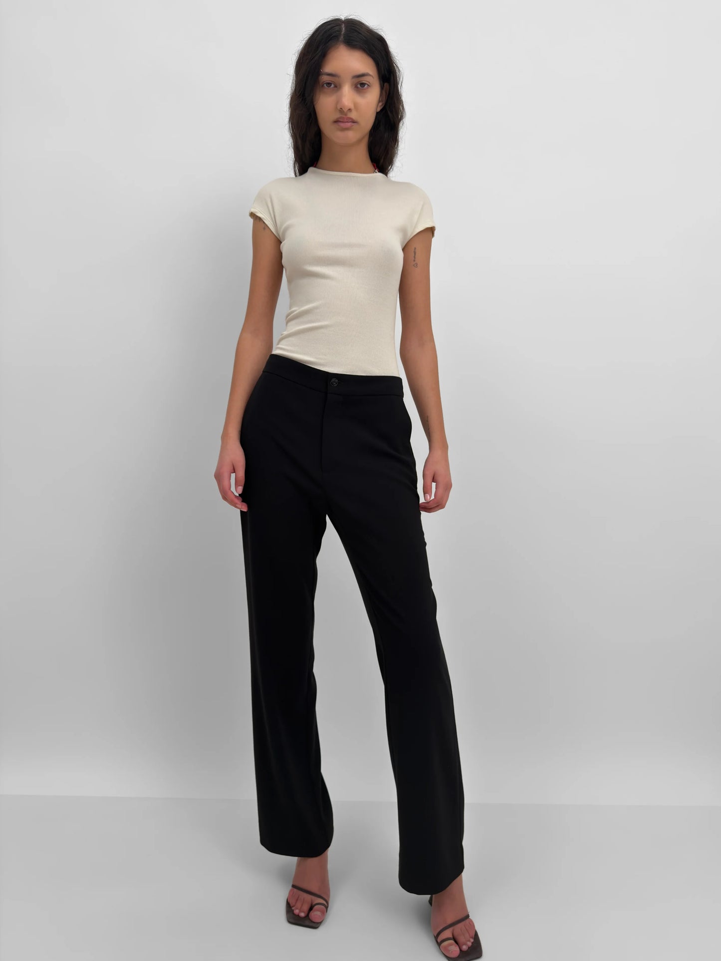 Woman wearing a beige top and black pants on a white background