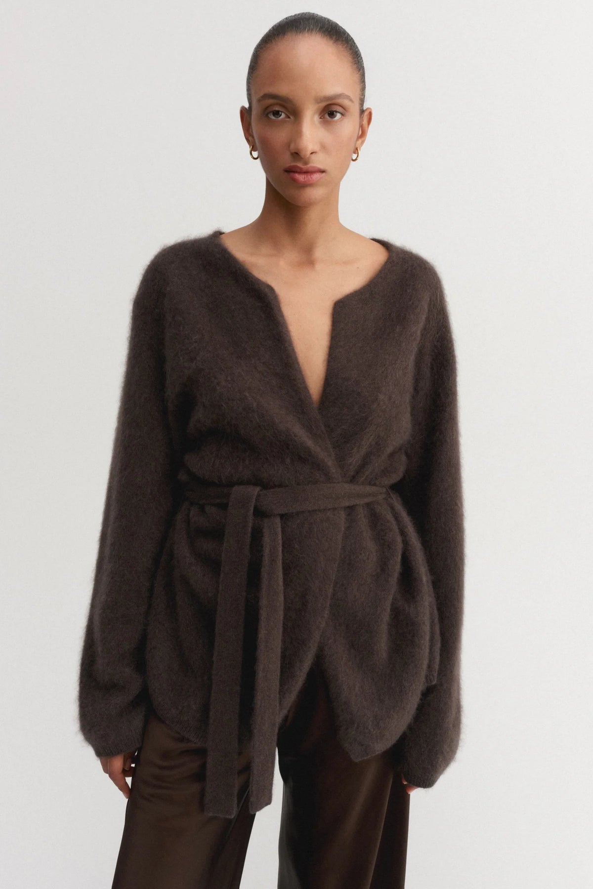 Woman wearing a brown wrap-style sweater with a belt on a white background