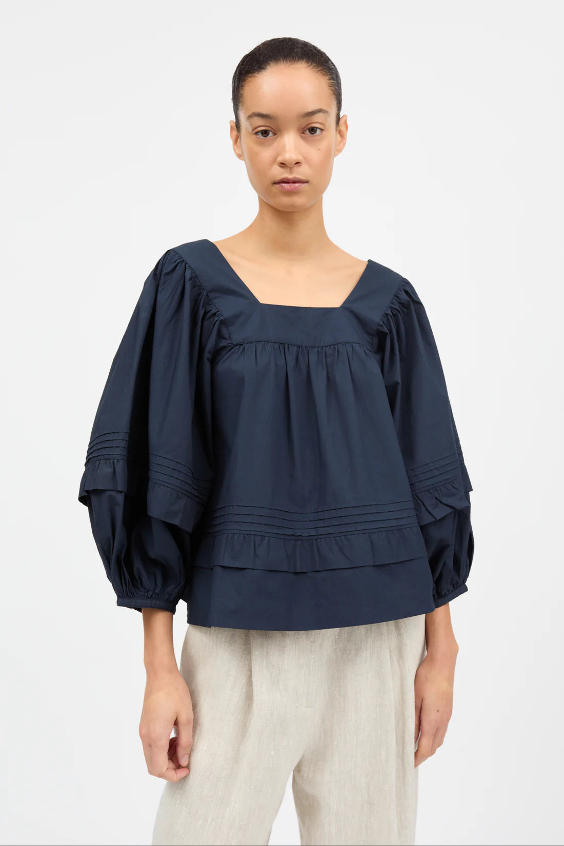 Woman wearing a navy blue blouse with ruffled sleeves on a white background