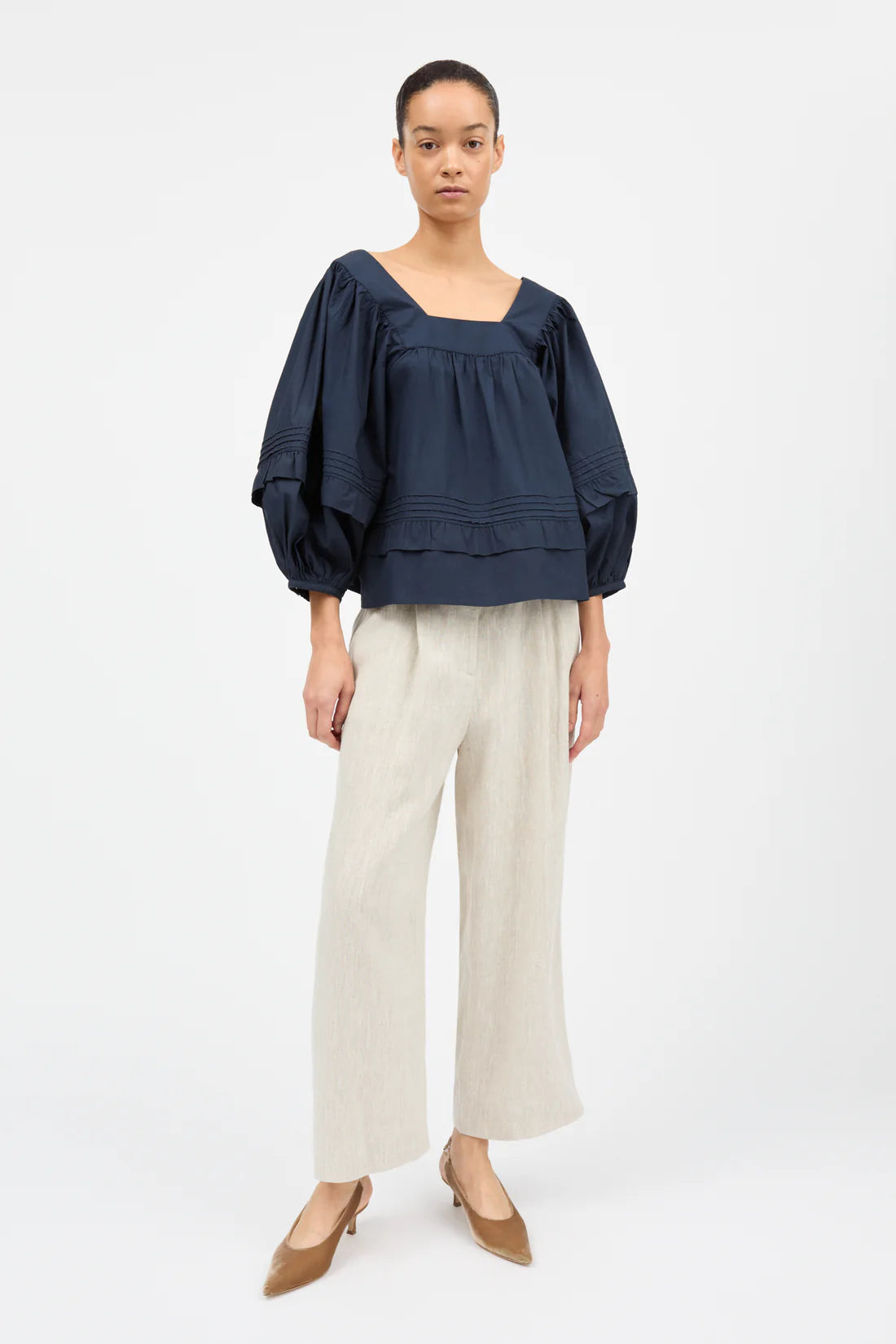 Woman wearing a navy blue top and beige pants on a white background