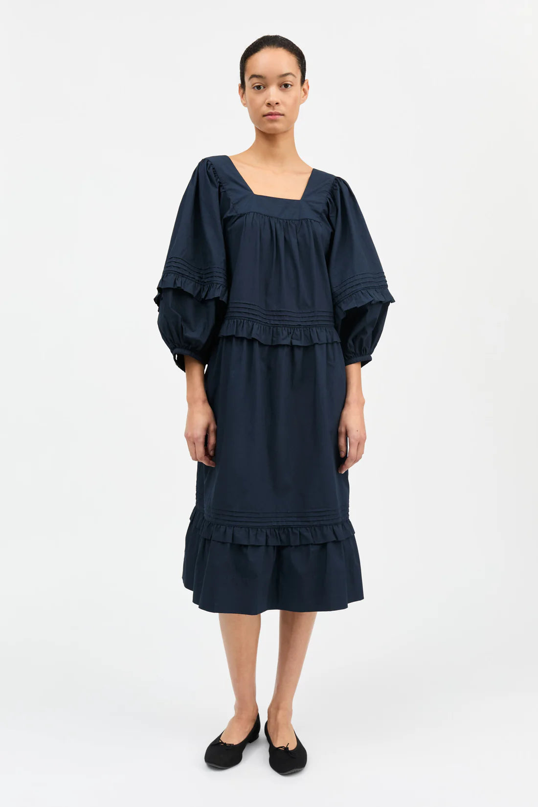 Woman wearing a navy blue dress with ruffled sleeves and hem on a white background
