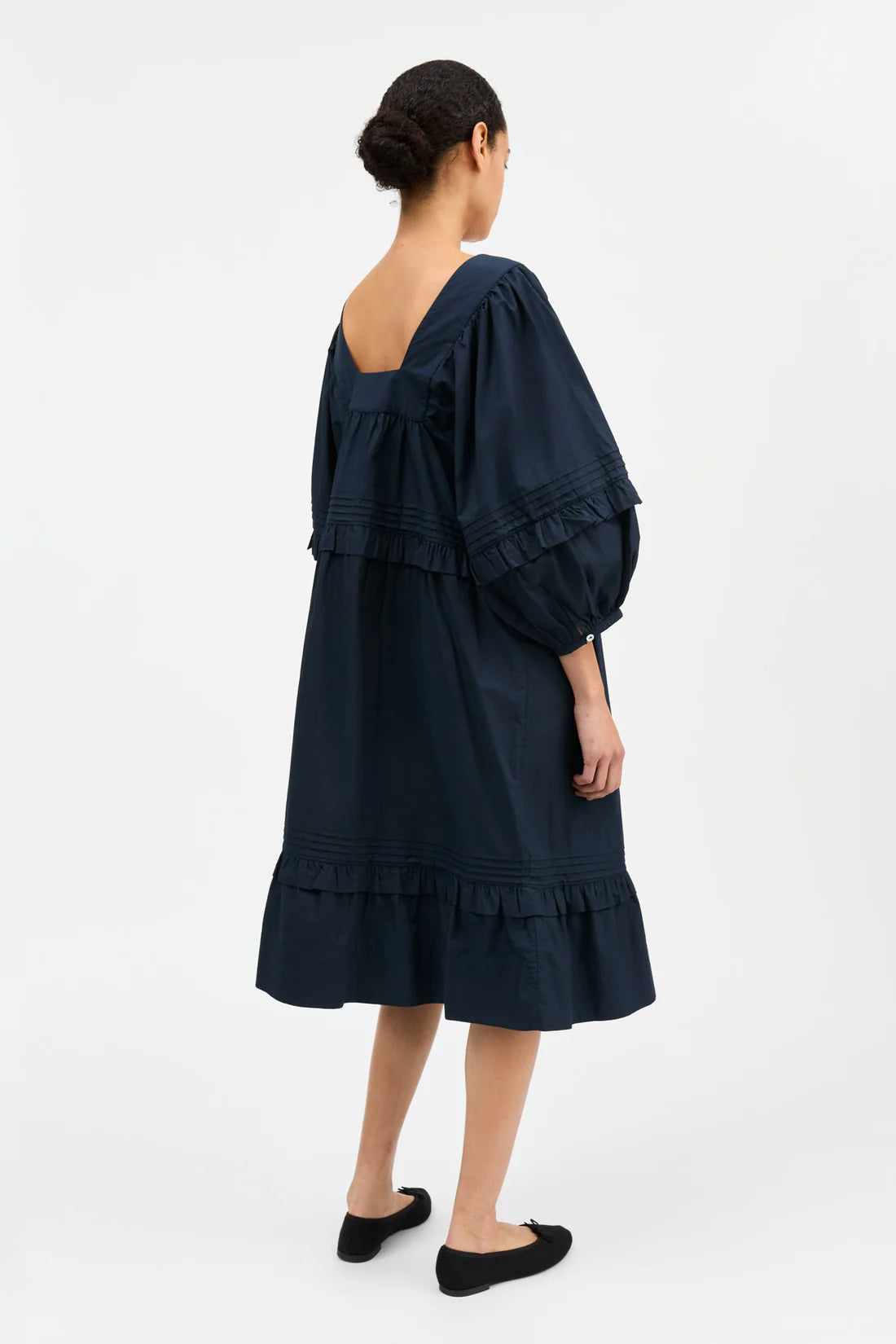 Woman wearing a dark blue dress with ruffled layers on a white background