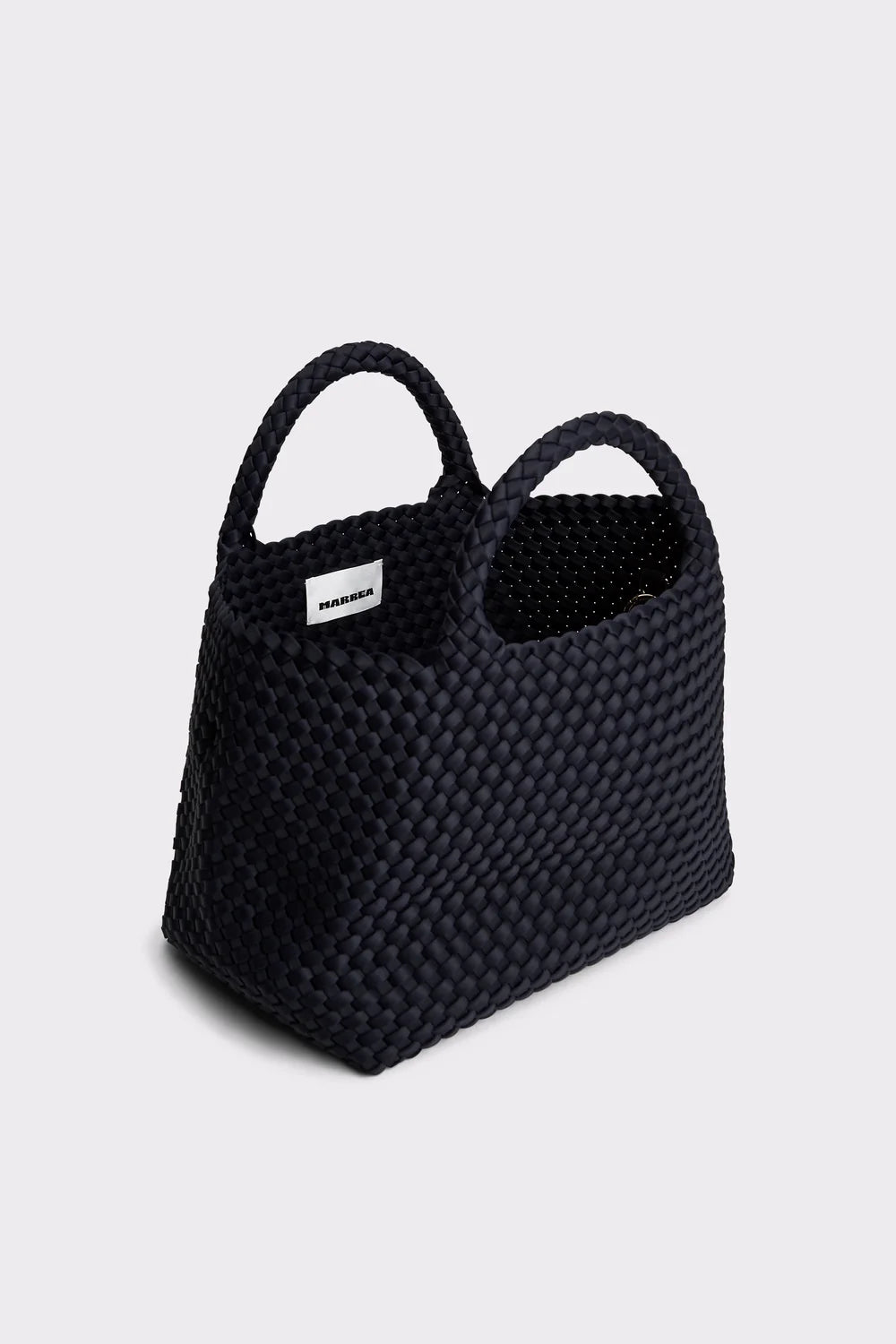 A black woven tote bag with two top handles and a small white brand label, photographed on a light gray background.