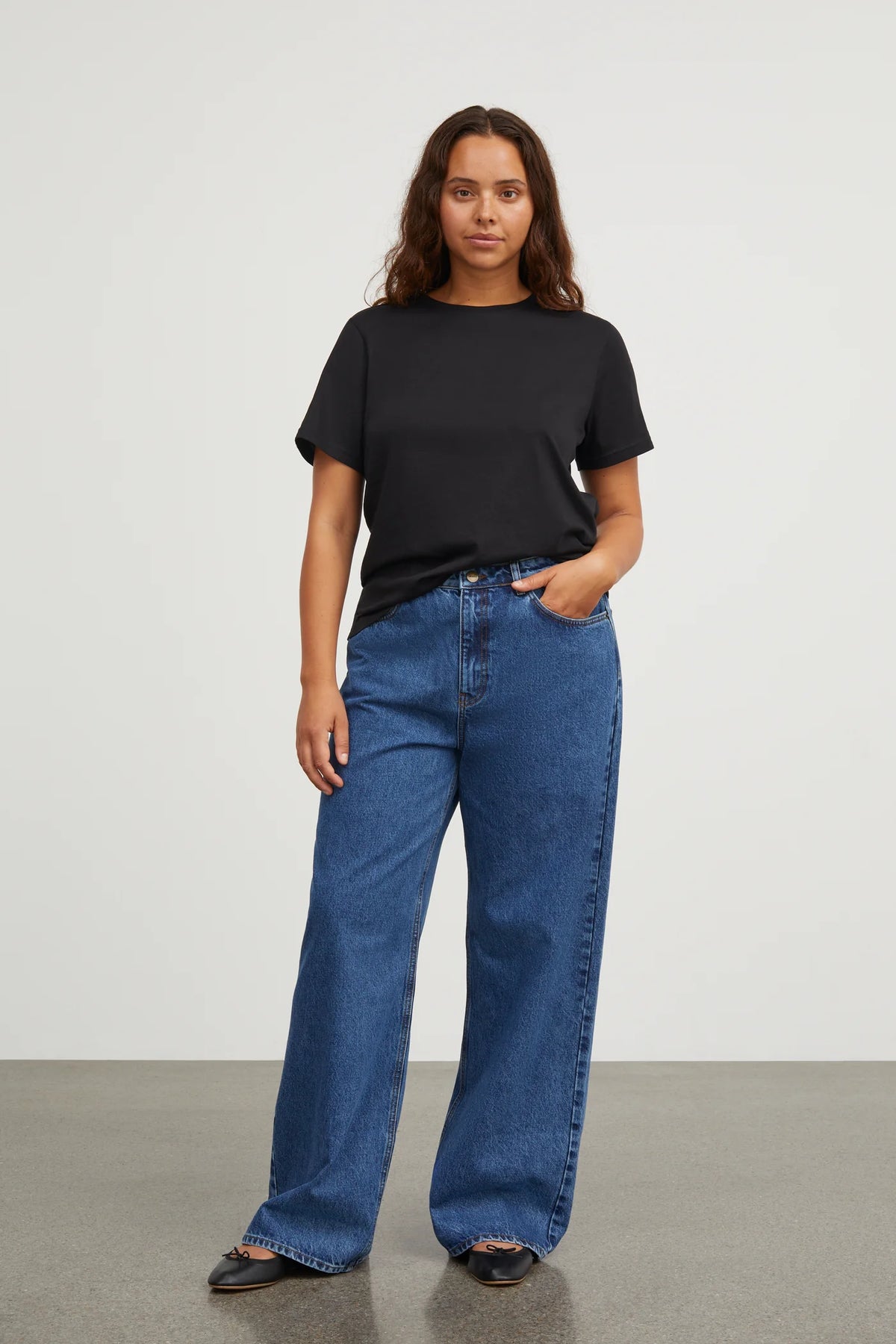 Woman wearing a black t-shirt and blue jeans against a white background