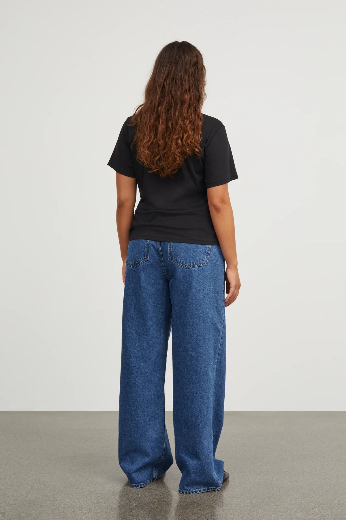 Person wearing a black t-shirt and blue jeans standing against a plain white background