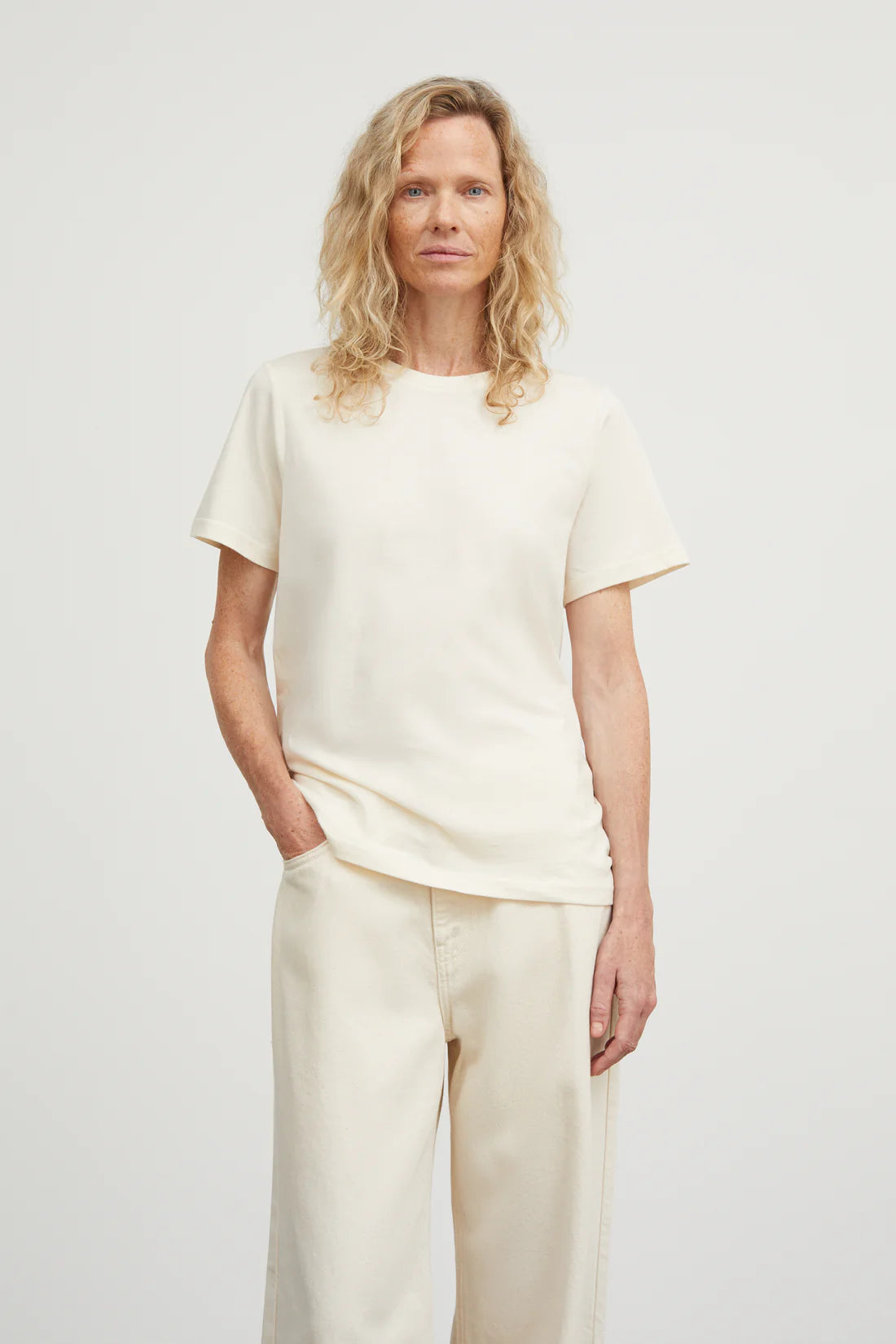 Woman wearing a white t-shirt and beige pants against a plain background