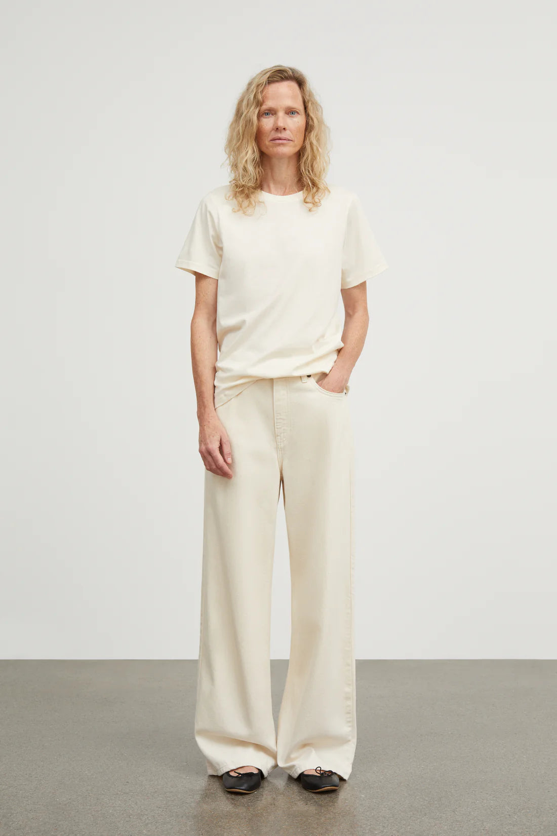 Woman wearing a white t-shirt and cream pants against a plain background