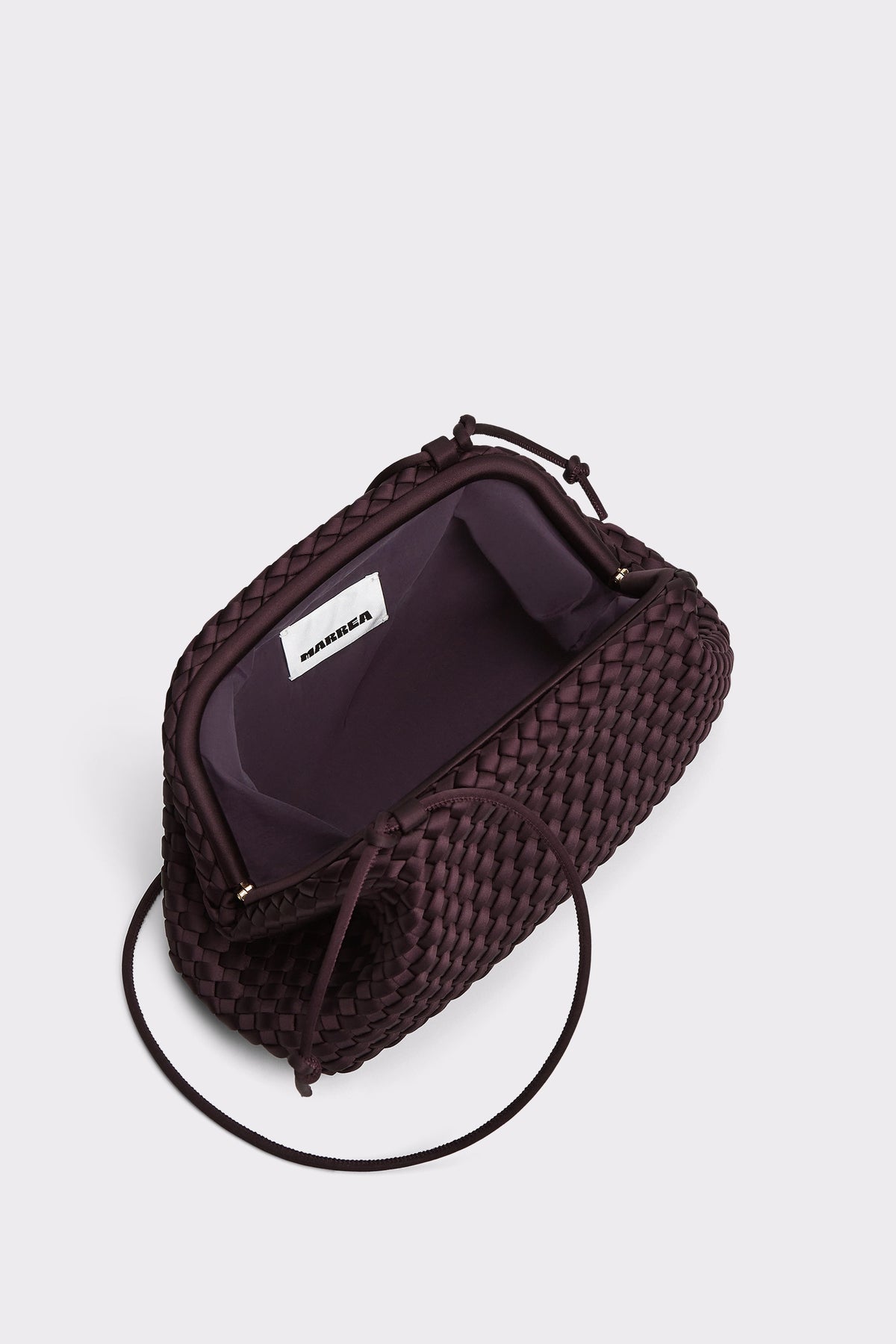 A dark brown woven leather clutch bag with a matching shoulder strap, shown from an overhead angle on a light gray background. The bag is open, revealing a dark purple interior lining with a white interior label.