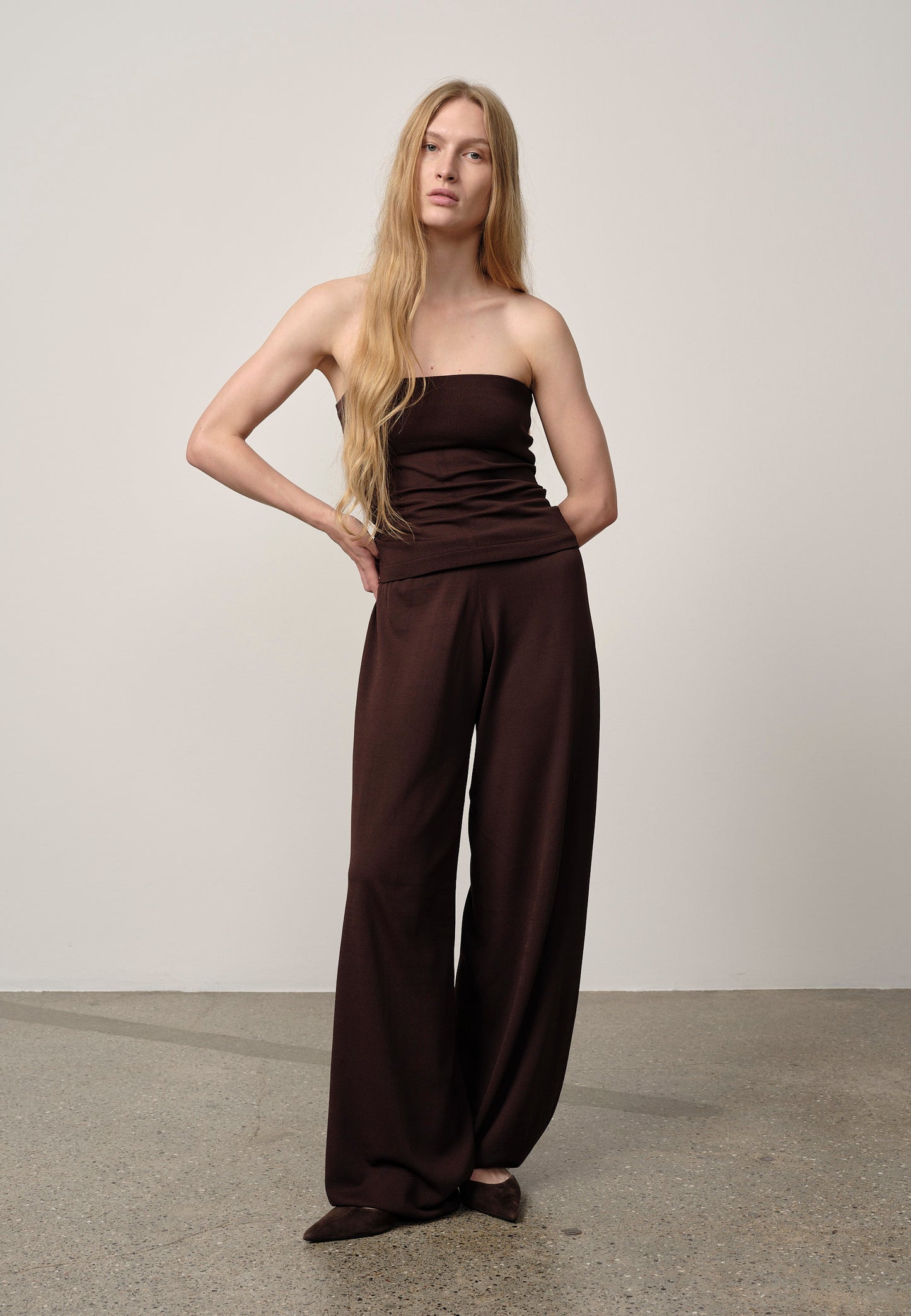 Woman wearing a brown strapless top and wide-leg pants against a plain background