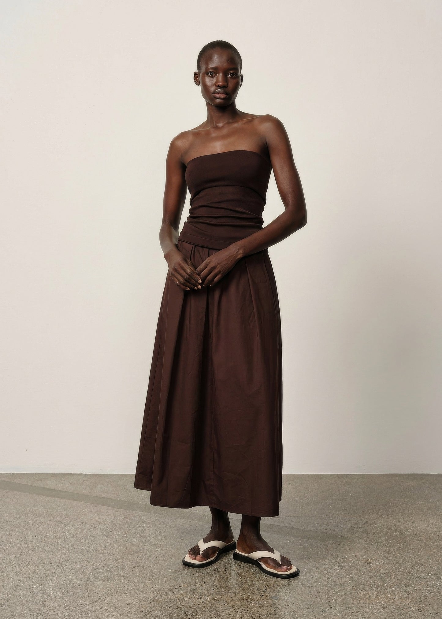 Woman wearing a brown strapless dress against a plain background