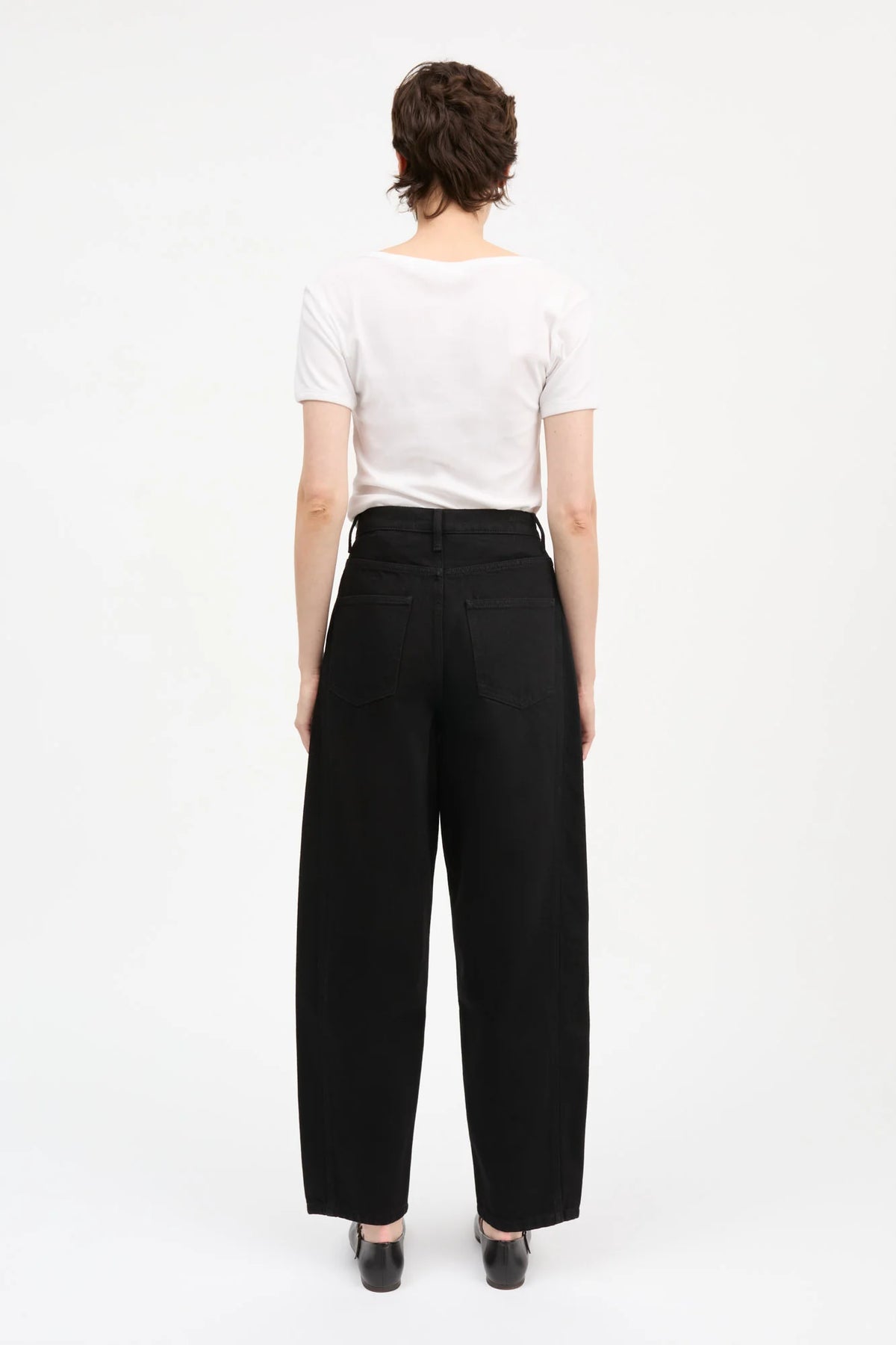 A model shown from the back wearing a white short-sleeve t-shirt and black wide-leg trousers, standing against a plain white studio background.