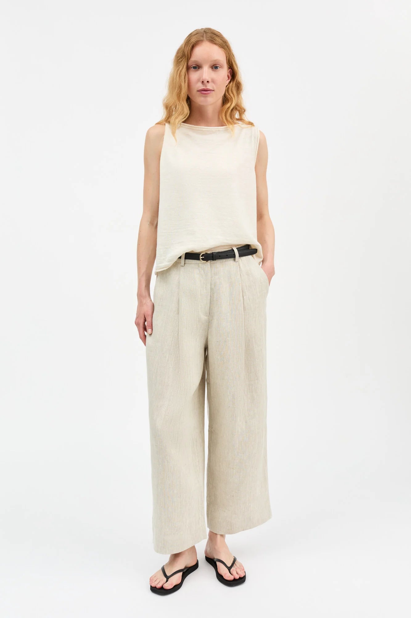 Woman wearing a sleeveless beige top and wide-leg pants on a white background