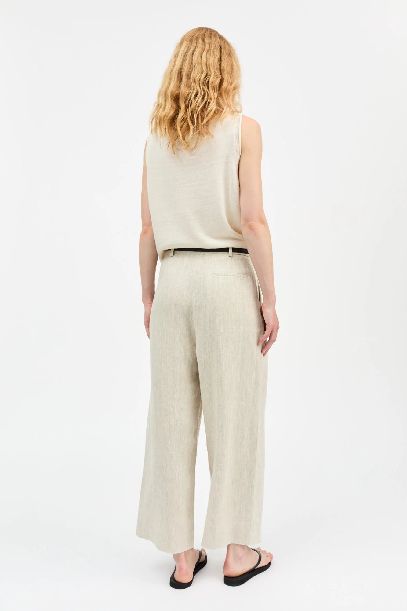Woman wearing a beige sleeveless top and wide-leg pants on a white background