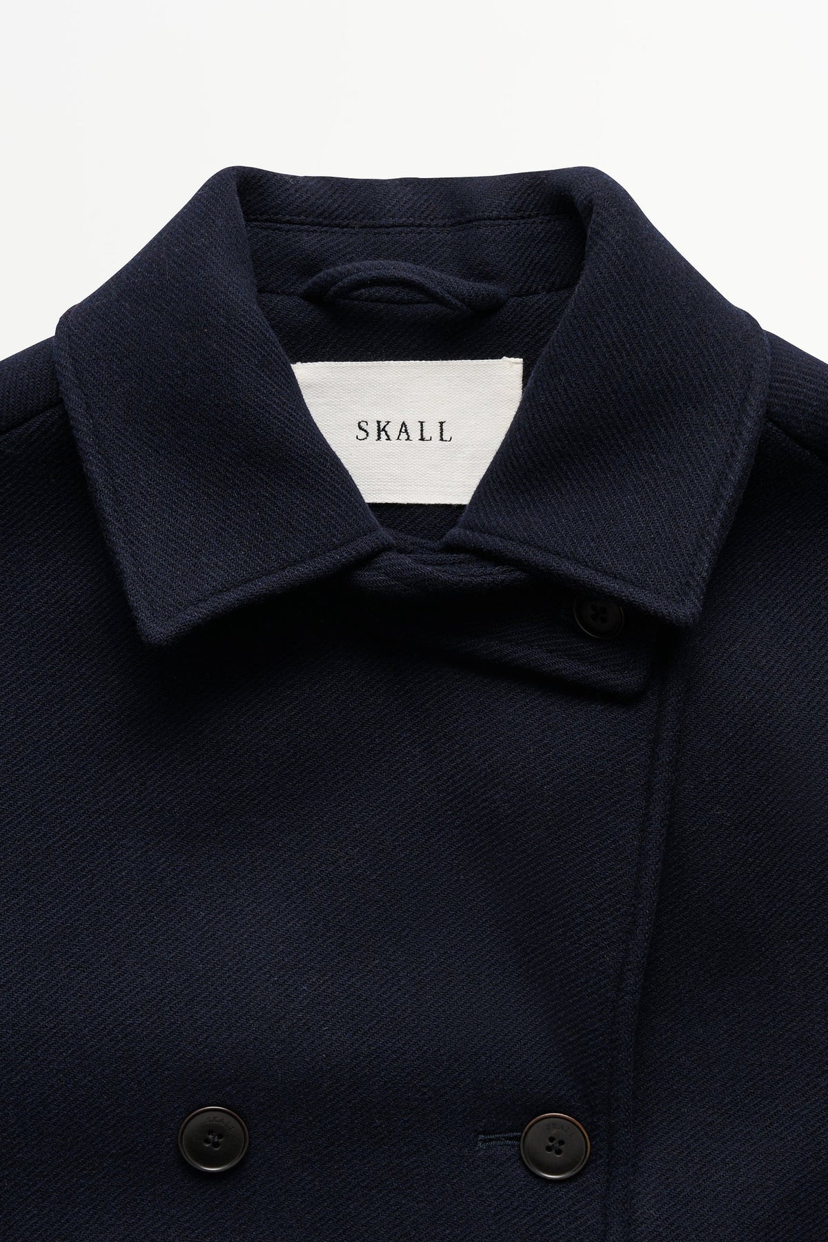 Close-up of a dark navy wool coat with a wide collar and a white interior neck label reading SKALL.