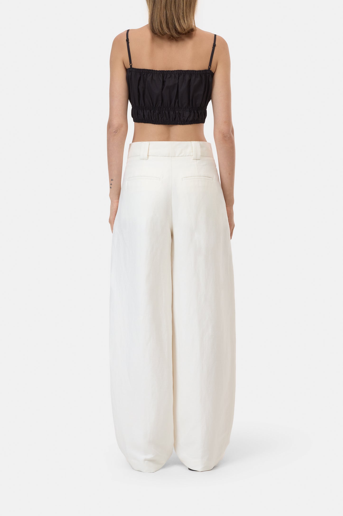 Person wearing a black crop top and white wide-leg pants on a white background