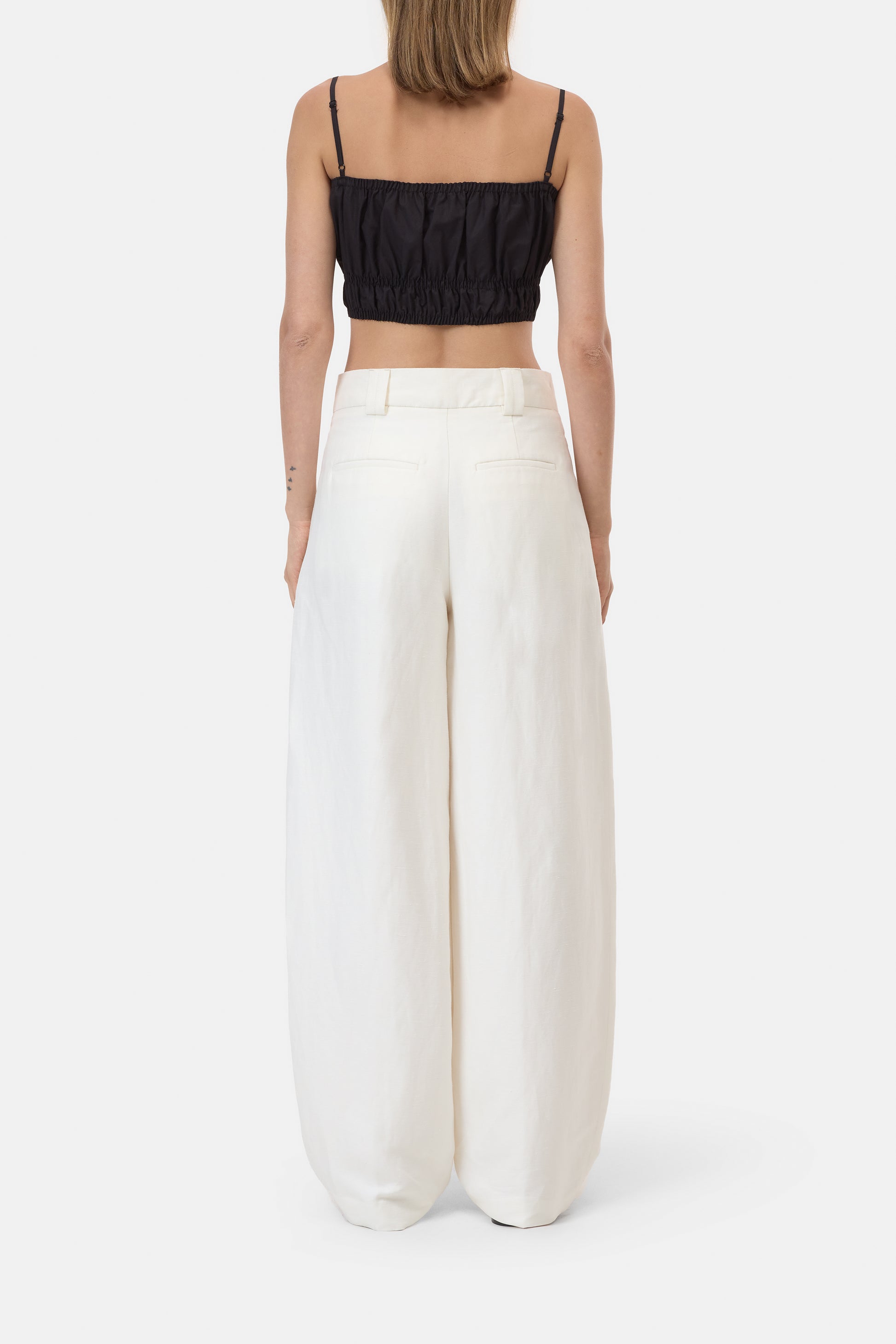Person wearing a black crop top and white wide-leg pants on a white background