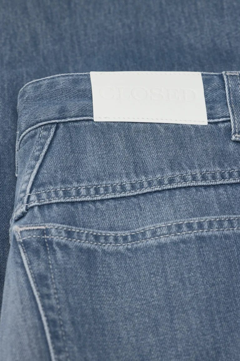 Close-up of the back waistband of light blue denim jeans, showing a white rectangular brand label that reads 'CLOSETED'.