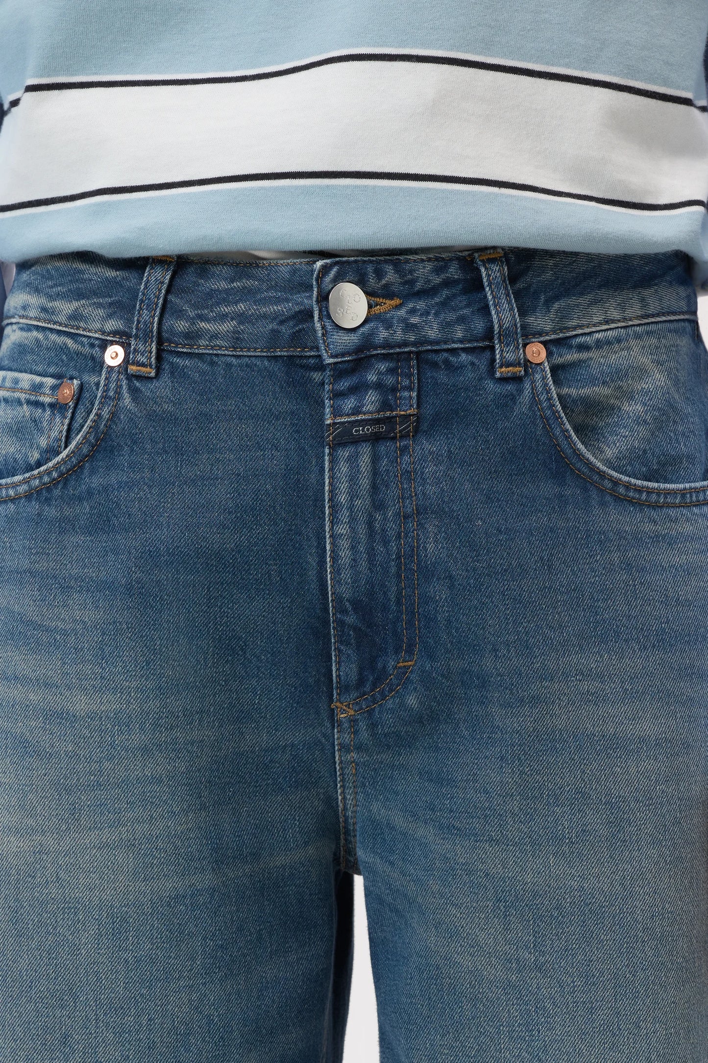 Close-up of a person wearing medium-wash blue denim jeans with a light blue and white striped top visible at the waist.
