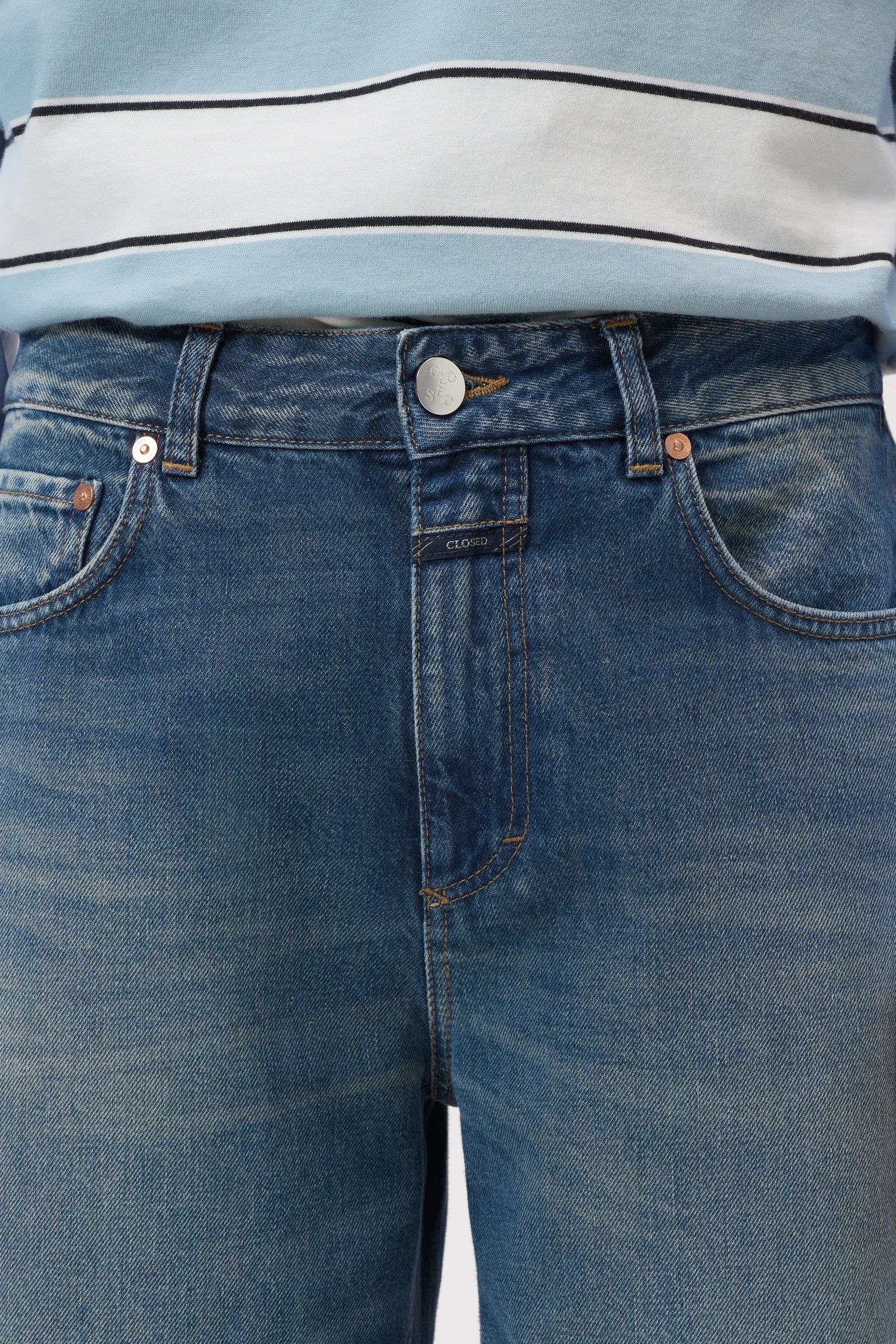 Close-up of a person wearing medium-wash blue denim jeans with a light blue and white striped top visible at the waist.