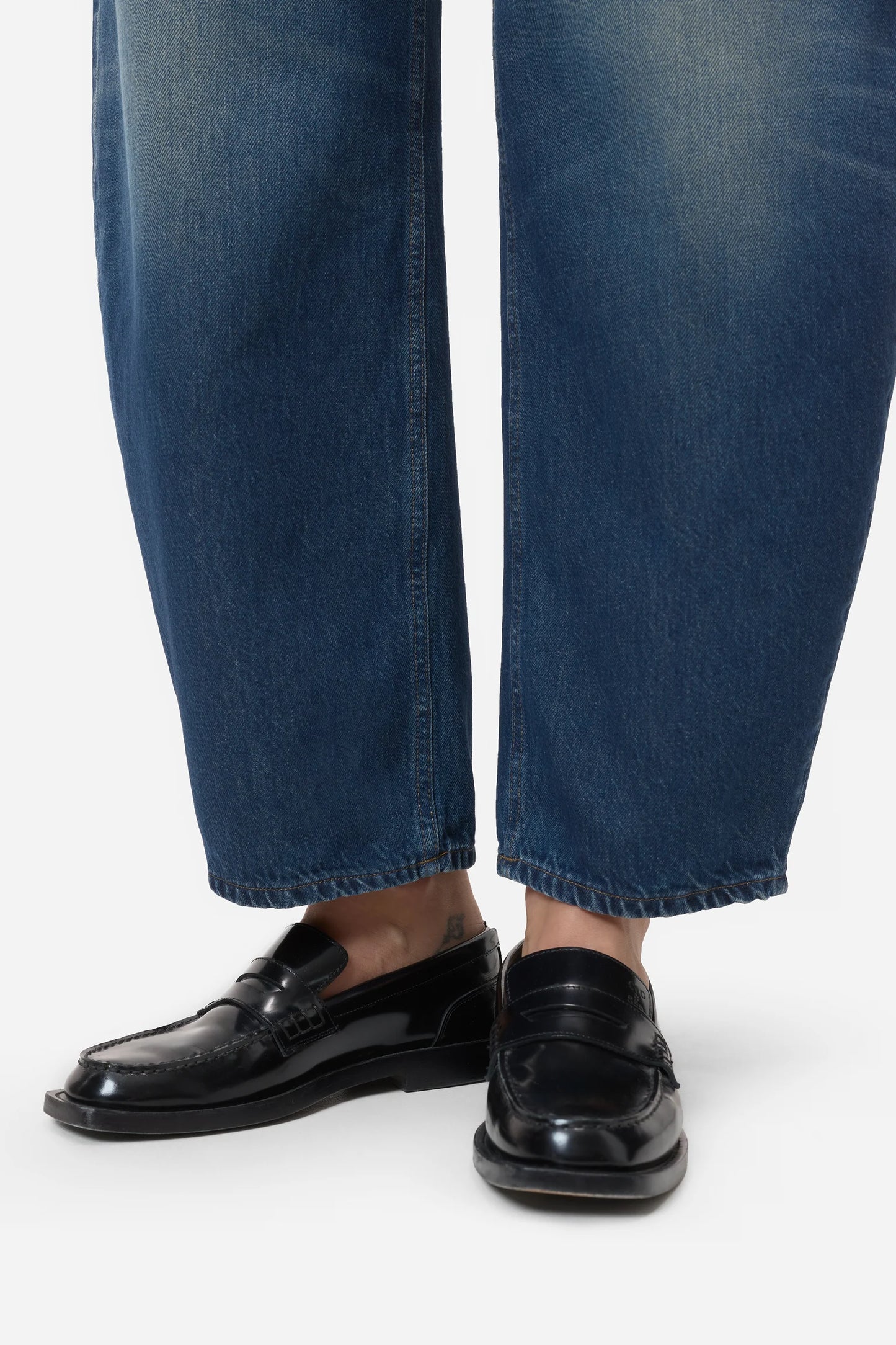 Person wearing black loafers and blue jeans on a white background