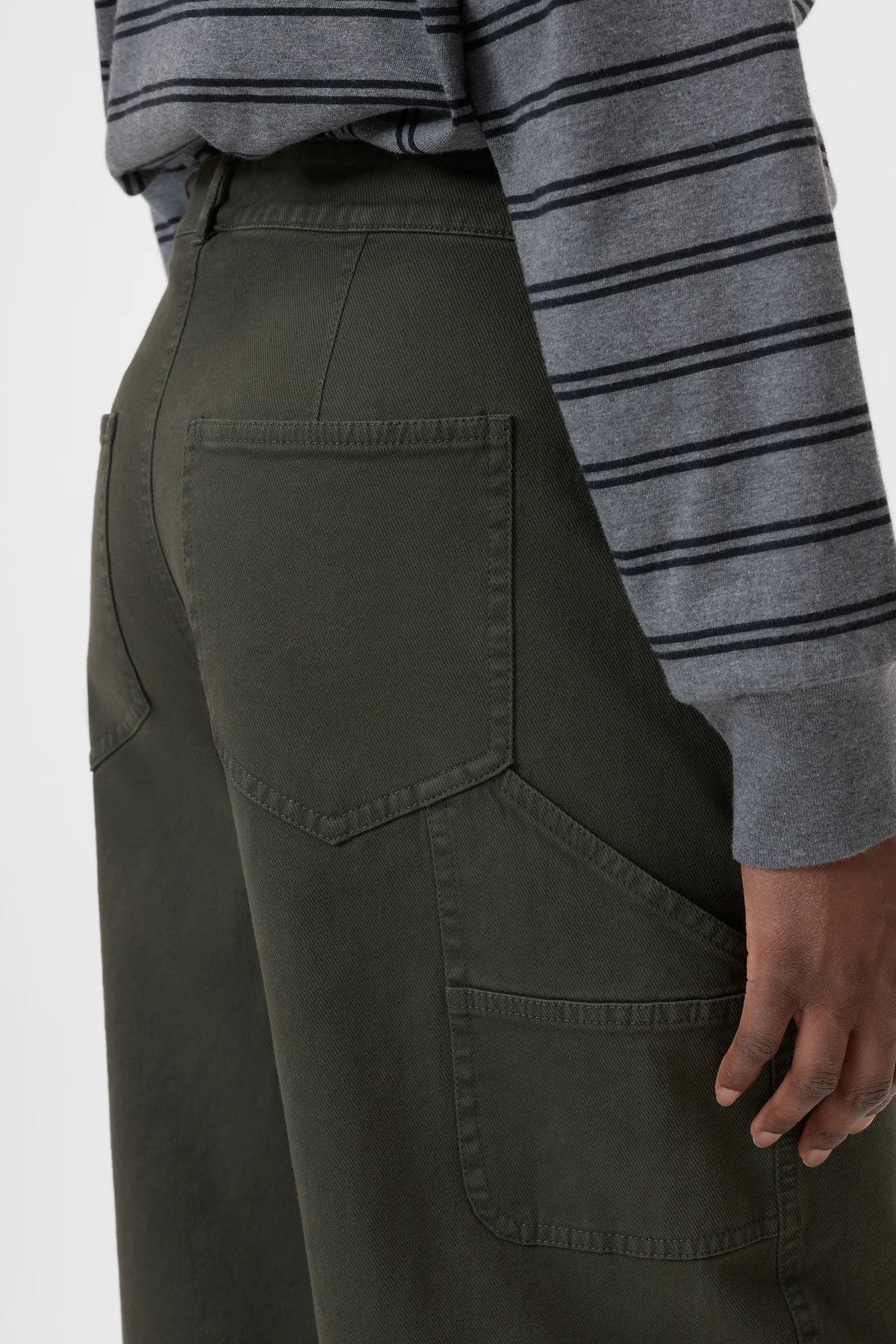 Person wearing dark green pants with a gray and black striped long-sleeve shirt on a white background
