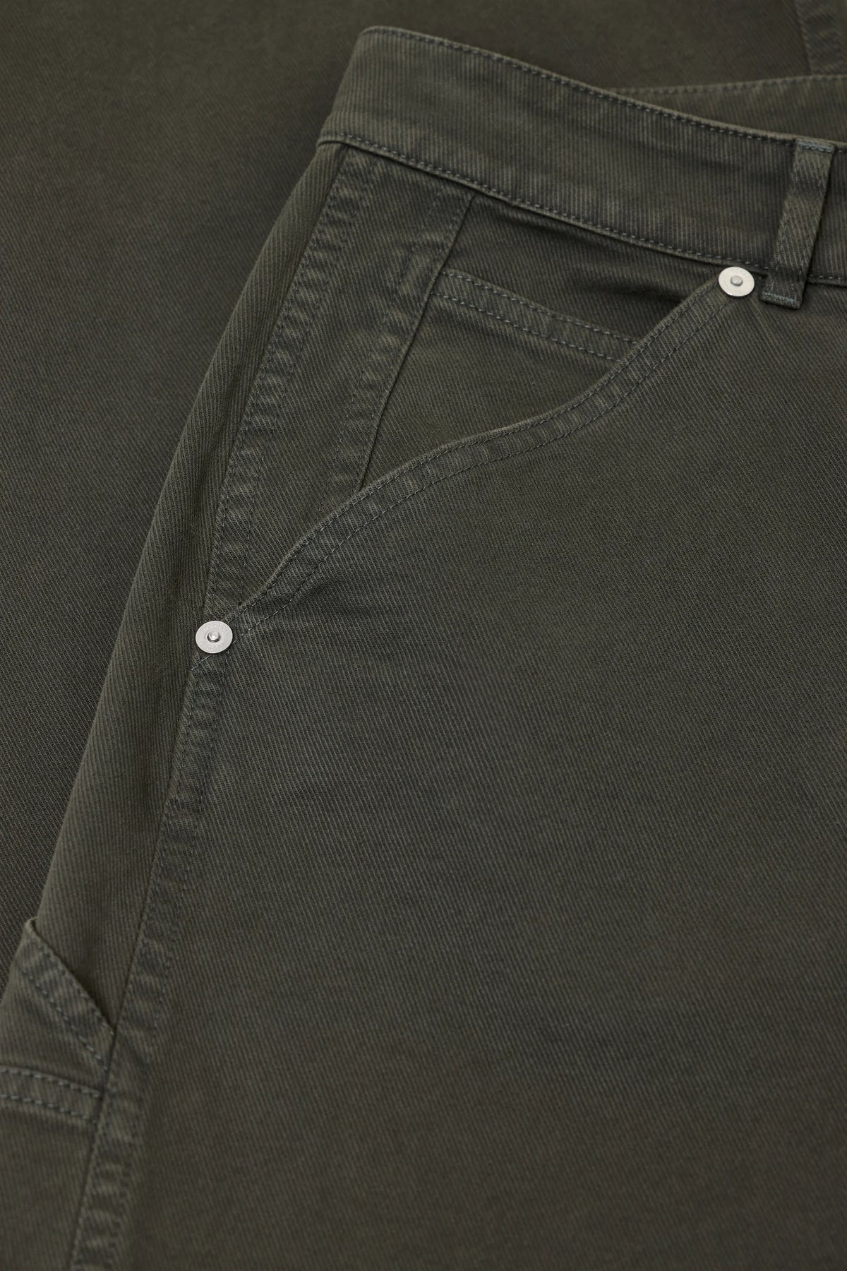 Close-up of olive green trousers showing the waistband, belt loop, side pocket, and silver-toned button details.