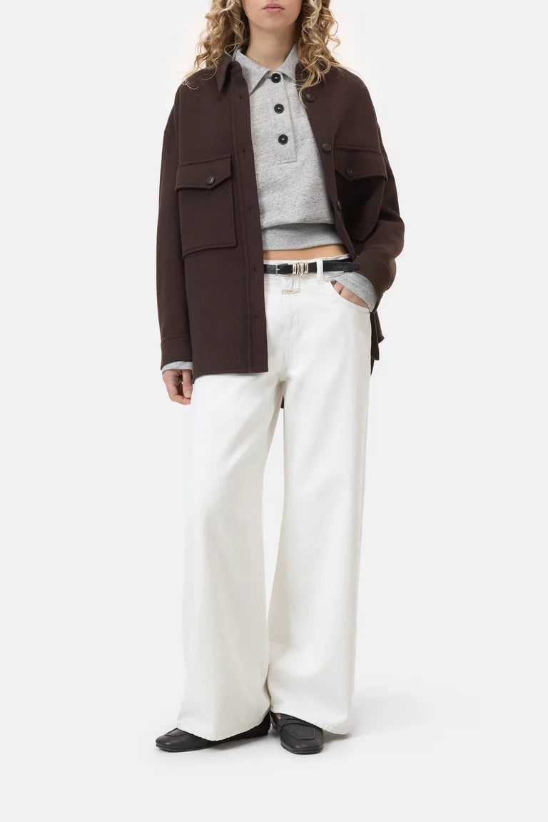 Person wearing a brown jacket, gray sweater, and white pants on a white background