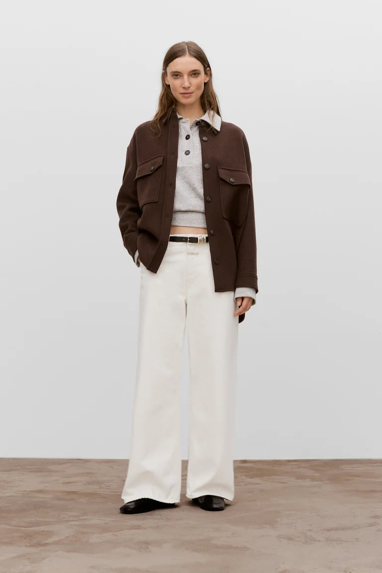 Woman wearing a brown jacket, white shirt, and white pants on a plain background