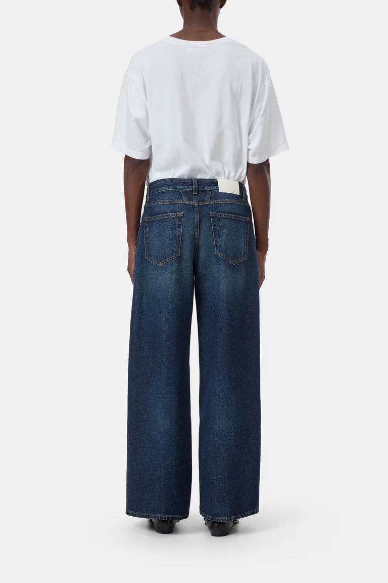 A model shown from the back wearing dark blue wide-leg denim jeans and a white t-shirt, standing against a plain light gray background.