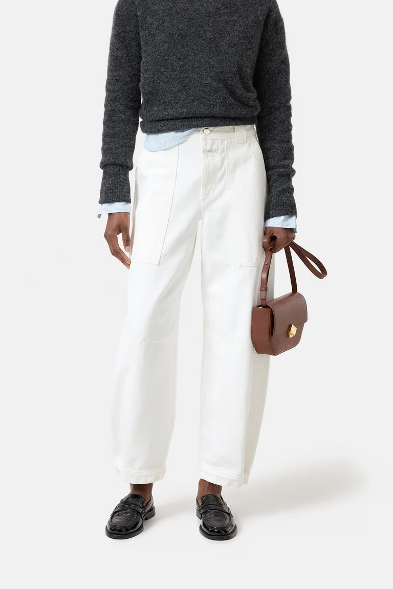 Person wearing a dark gray sweater, white pants, black shoes, and holding a brown handbag on a white background