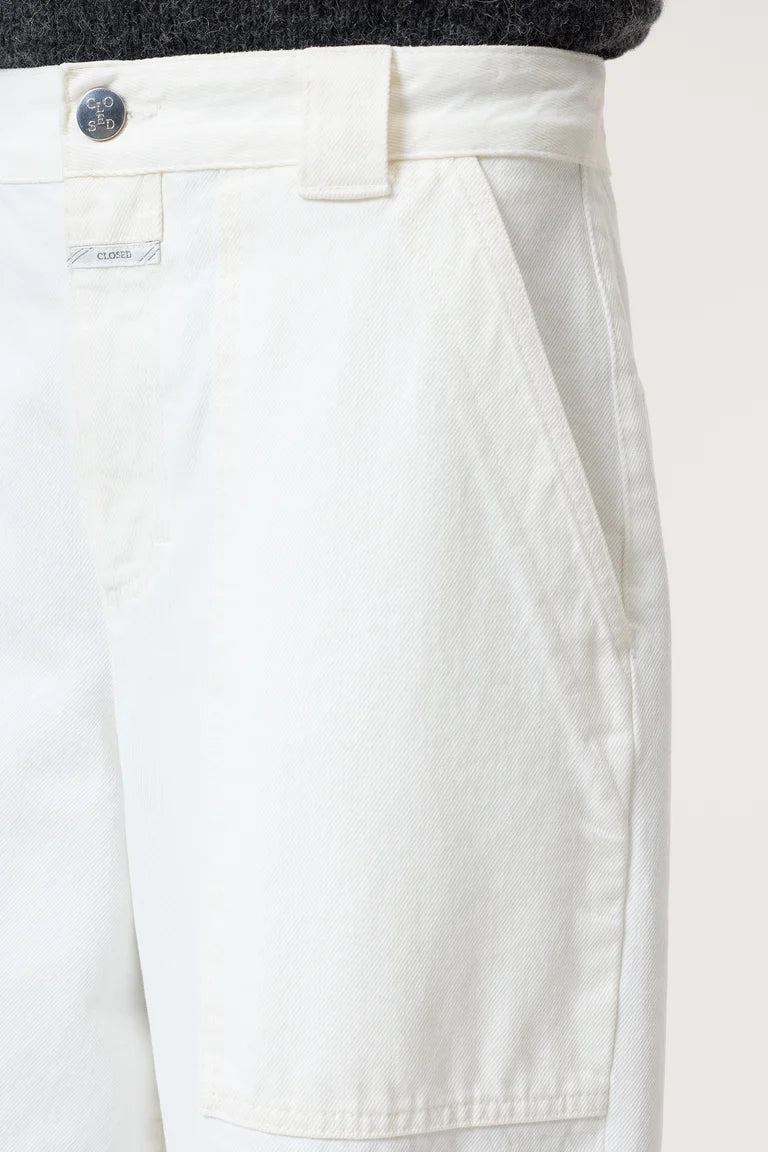 Close-up of white pants with a button and brand label on a light background