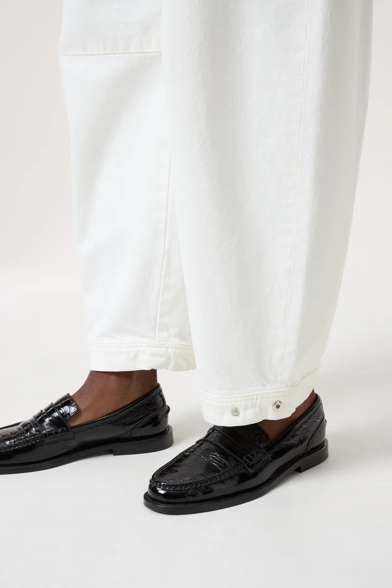 Black loafers worn with white pants on a light background
