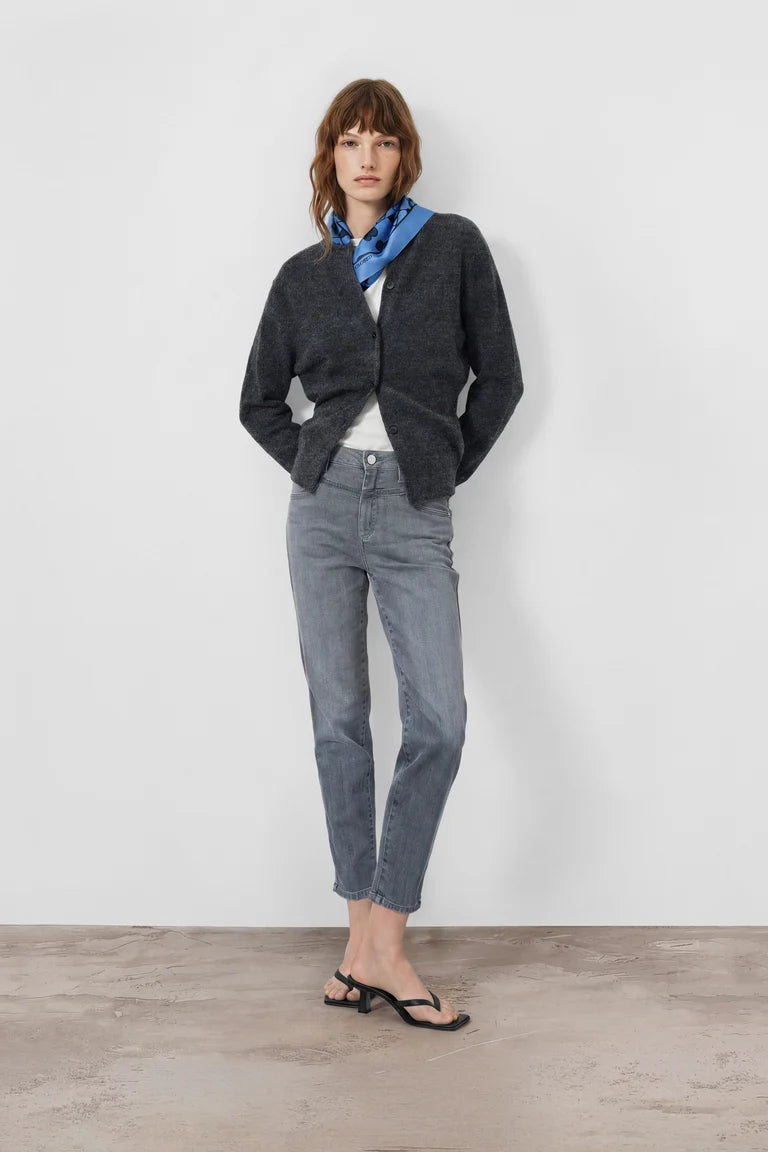 Person wearing a dark gray cardigan, light blue jeans, and black sandals on a white background