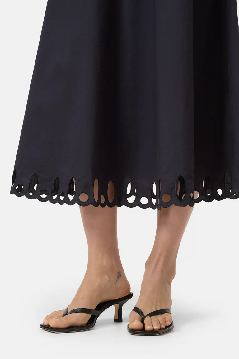 Person wearing a black dress with cut-out hem and black high-heeled sandals on a white background