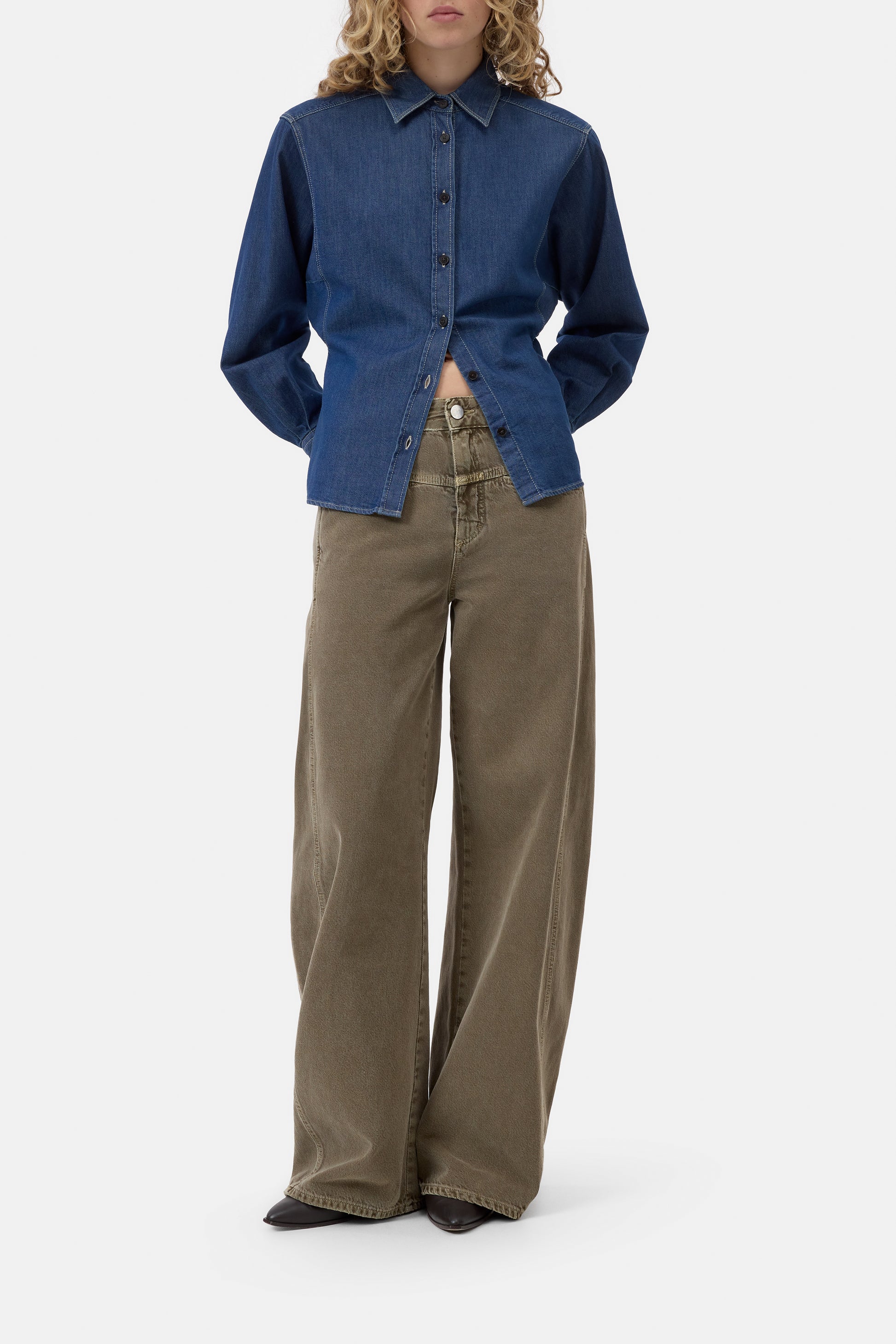 Person wearing a blue denim shirt and brown pants on a white background