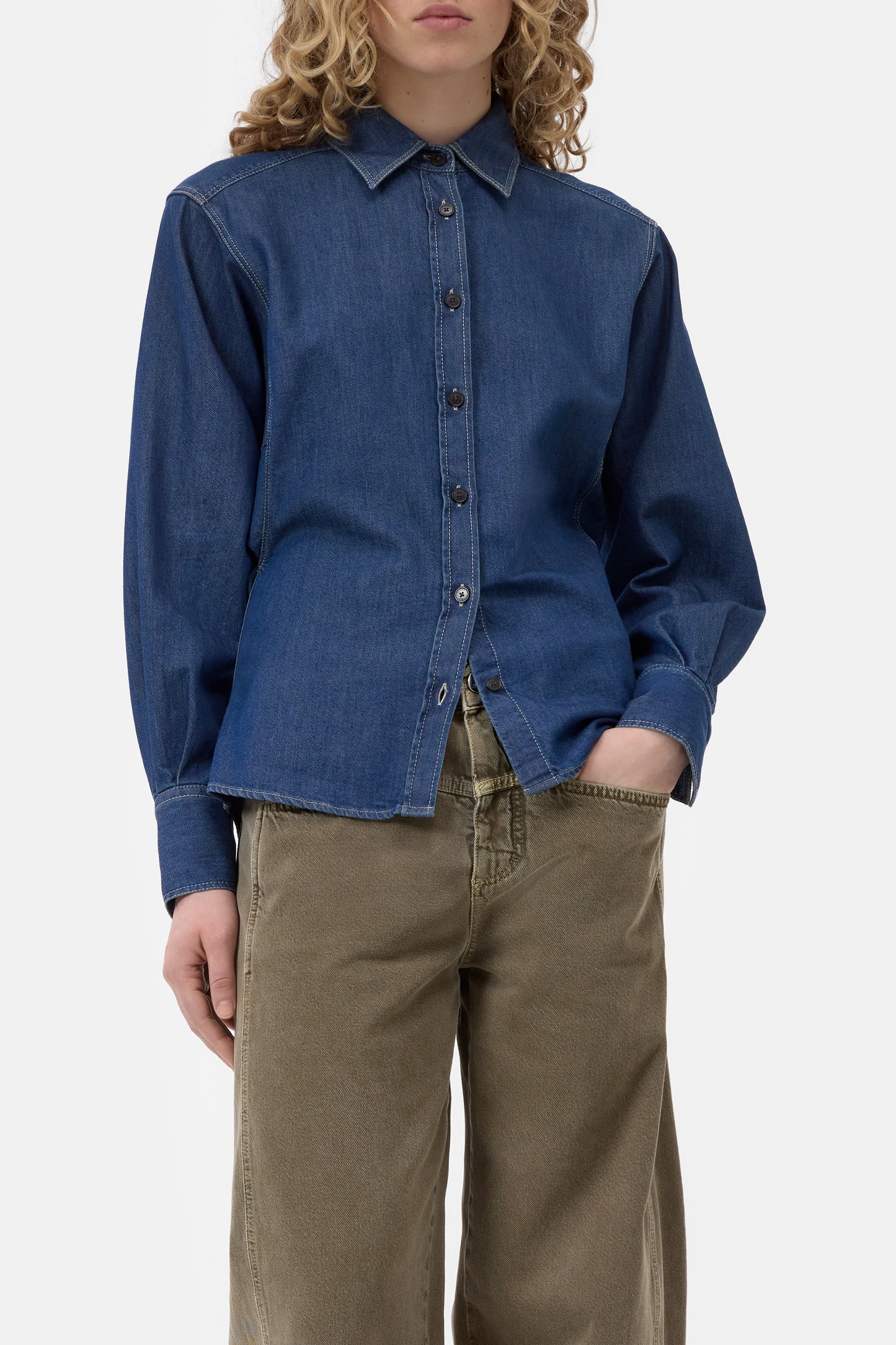 Person wearing a blue denim shirt and brown pants on a white background