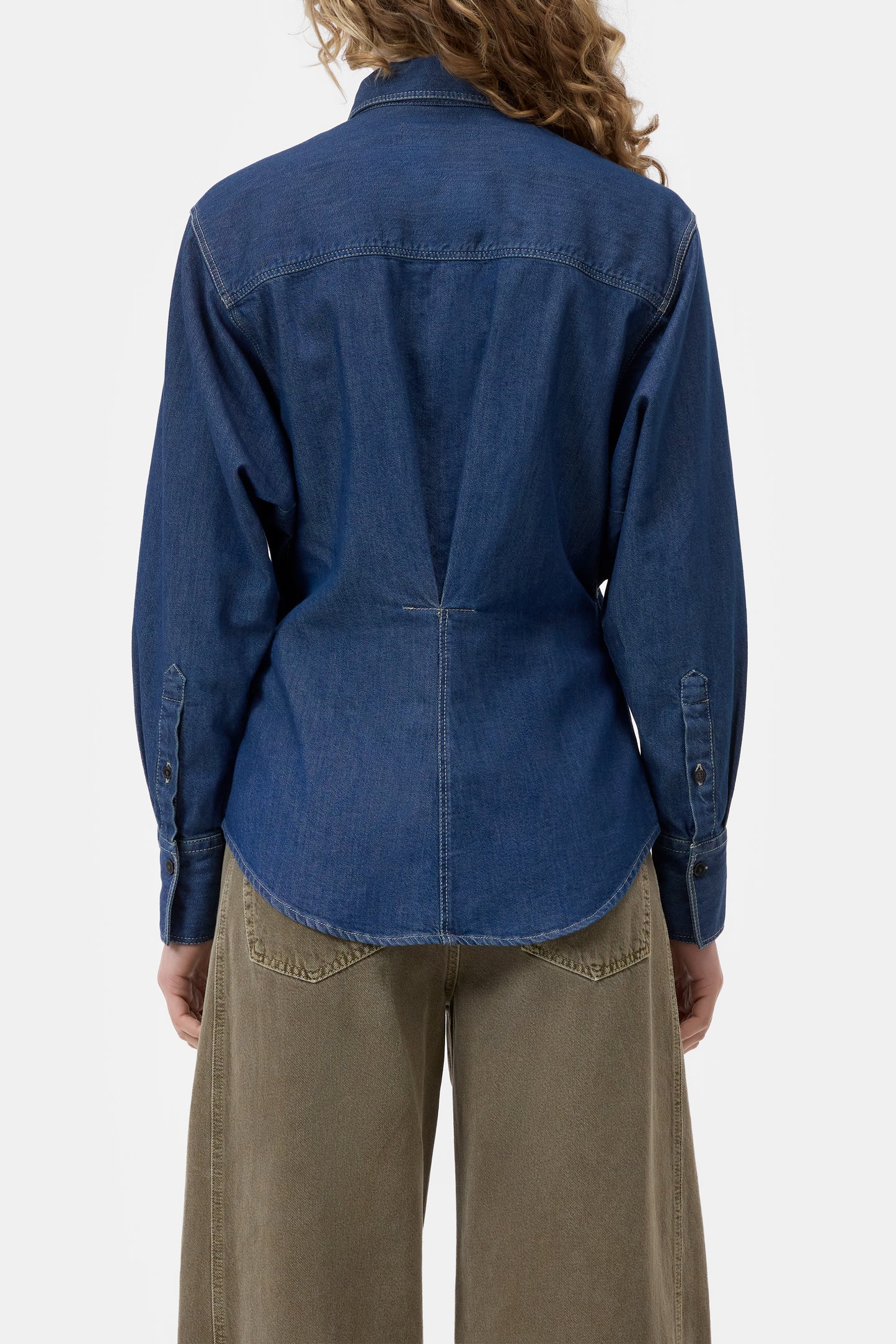 Person wearing a blue denim shirt and brown pants on a white background