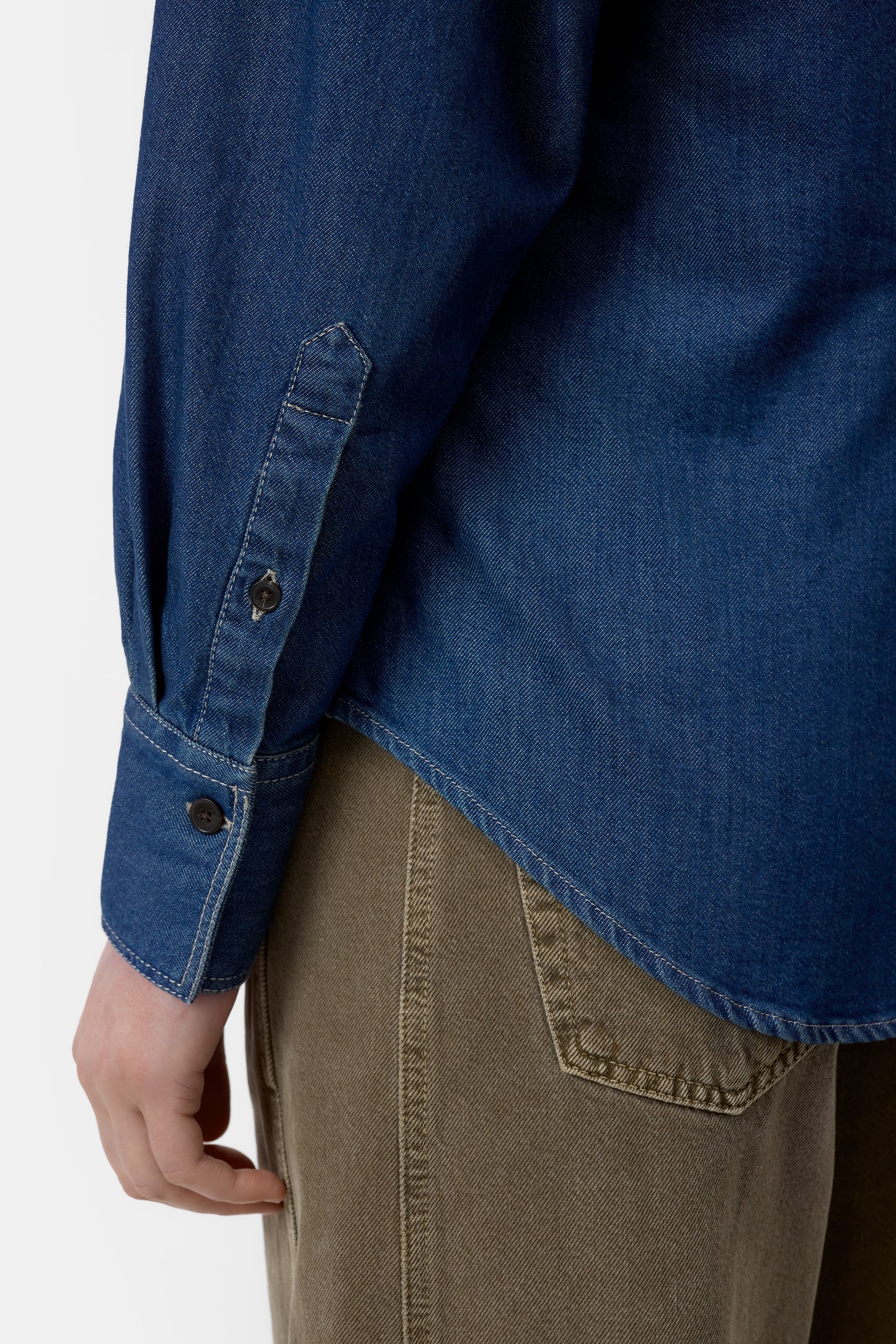 Blue denim shirt with rolled-up sleeve and brown pants on a white background