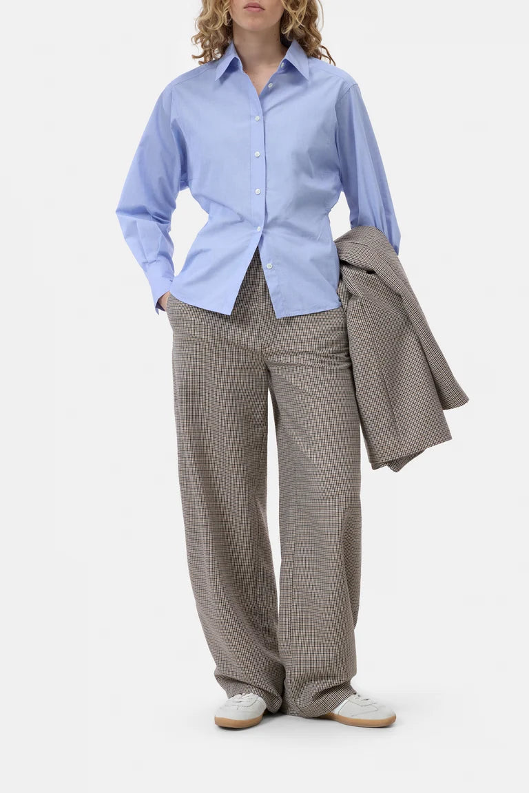 Person wearing a light blue shirt and brown checkered pants with a gray jacket on a white background