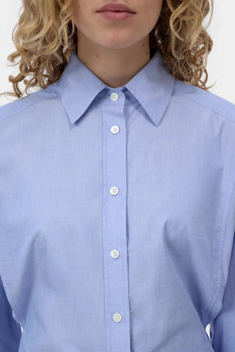 A close-up of a model wearing a light blue button-down shirt with a classic collar and white buttons.