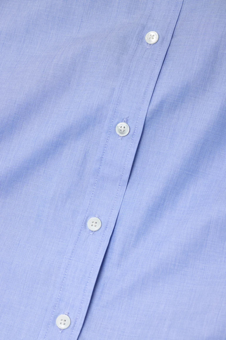 Close-up of a light blue button-down shirt fabric with white buttons along the placket.