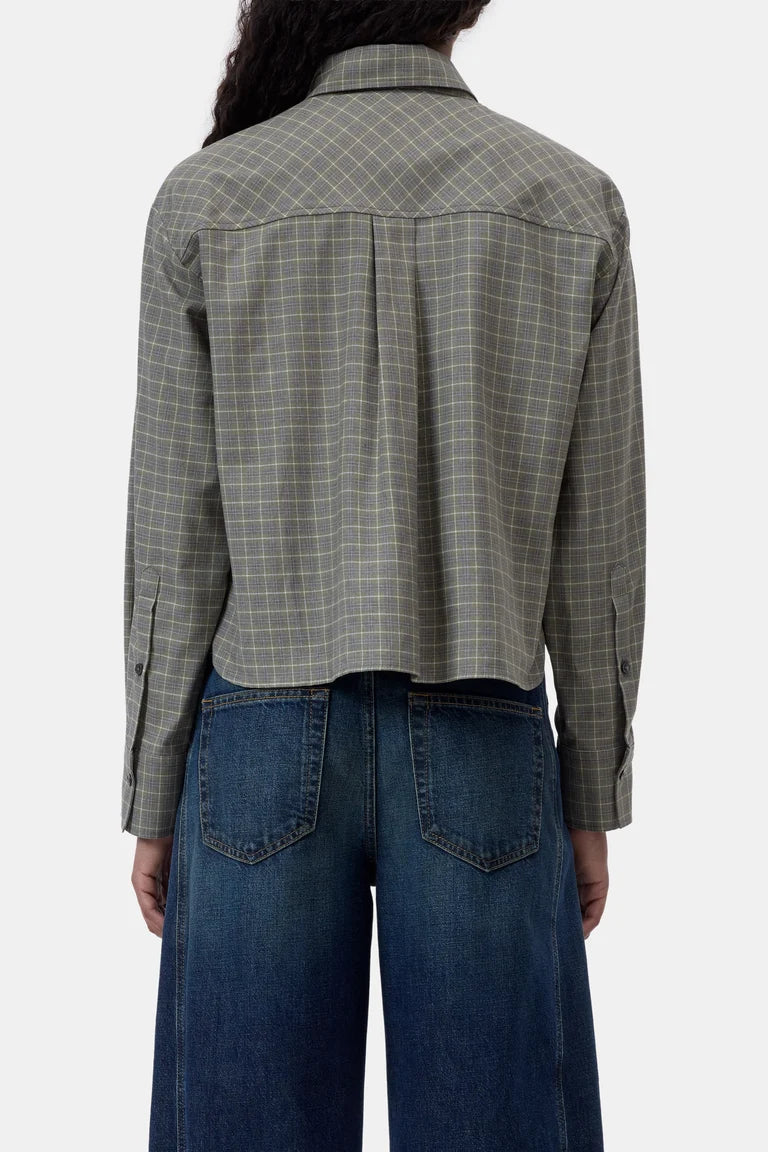A person shown from the back wearing a cropped long-sleeve plaid shirt in muted green-gray with blue jeans, against a plain light background.