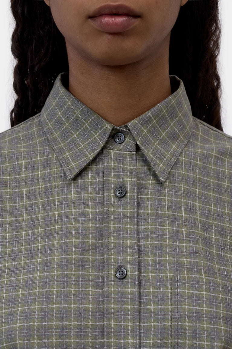 Close-up of a person wearing a collared button-front shirt with a muted green and gray plaid pattern.