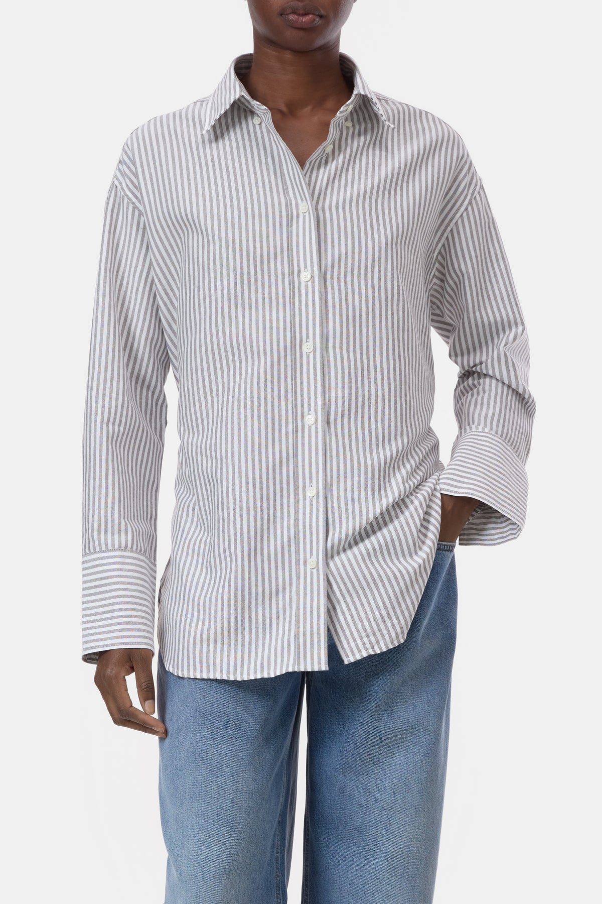 A model wearing a white long-sleeve button-up shirt with thin vertical gray stripes, paired with light blue jeans, against a plain light gray background.