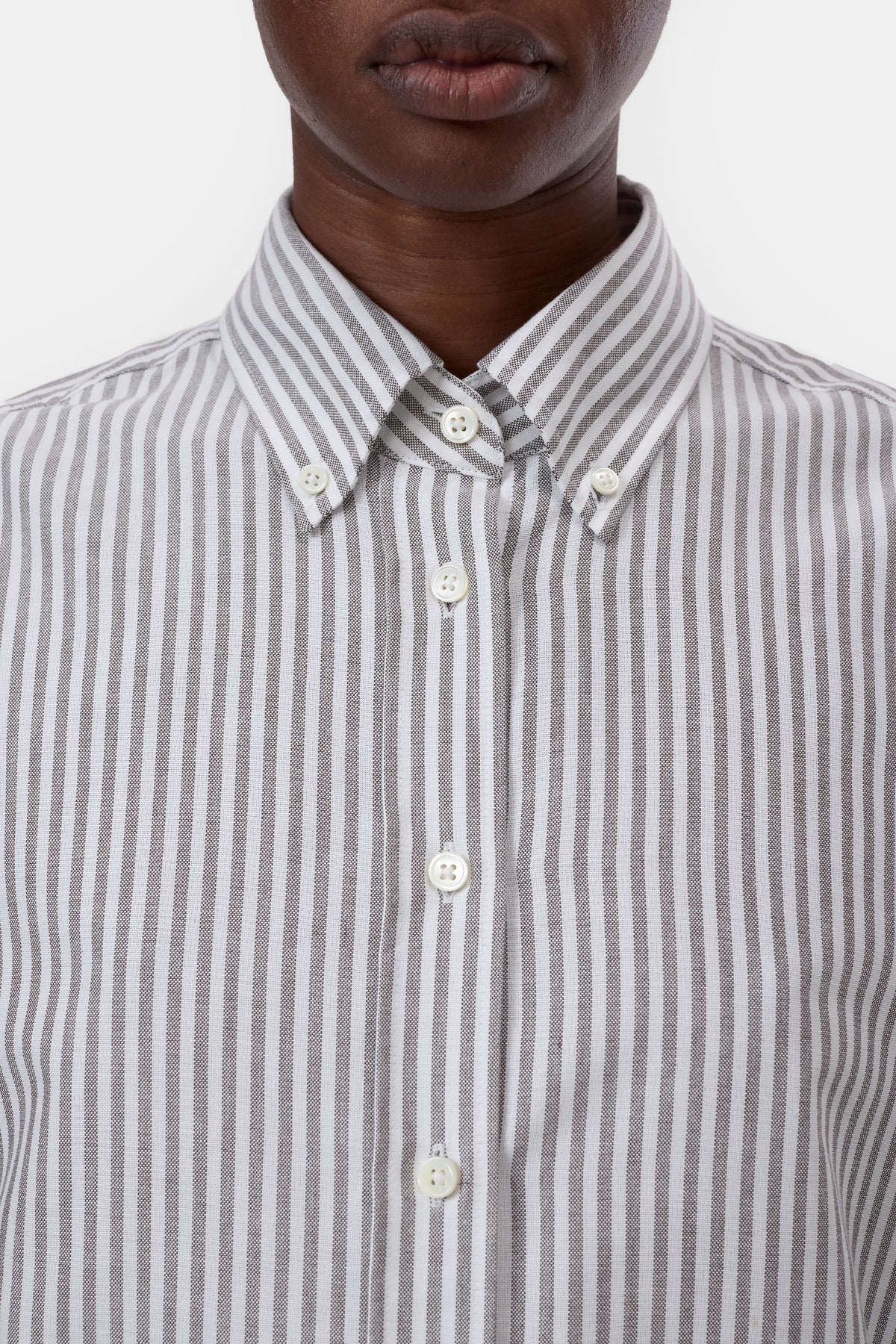 Close-up of a person wearing a gray and white vertically striped button-down shirt, showing the collar, front buttons, and chest area against a plain light background.